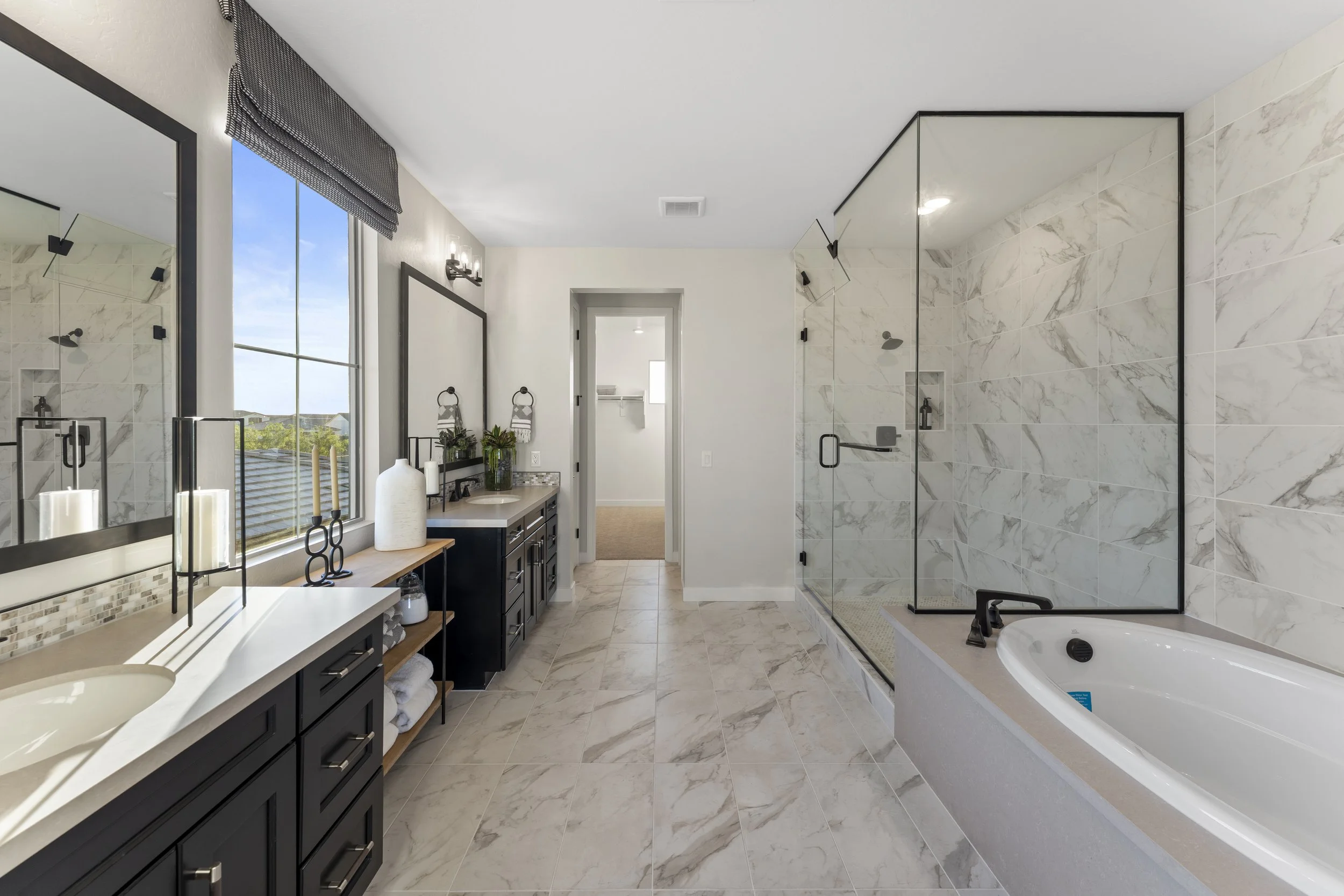 Modern bathroom with double sinks, large mirror, walk-in shower with glass doors, and bathtub with black fixtures.