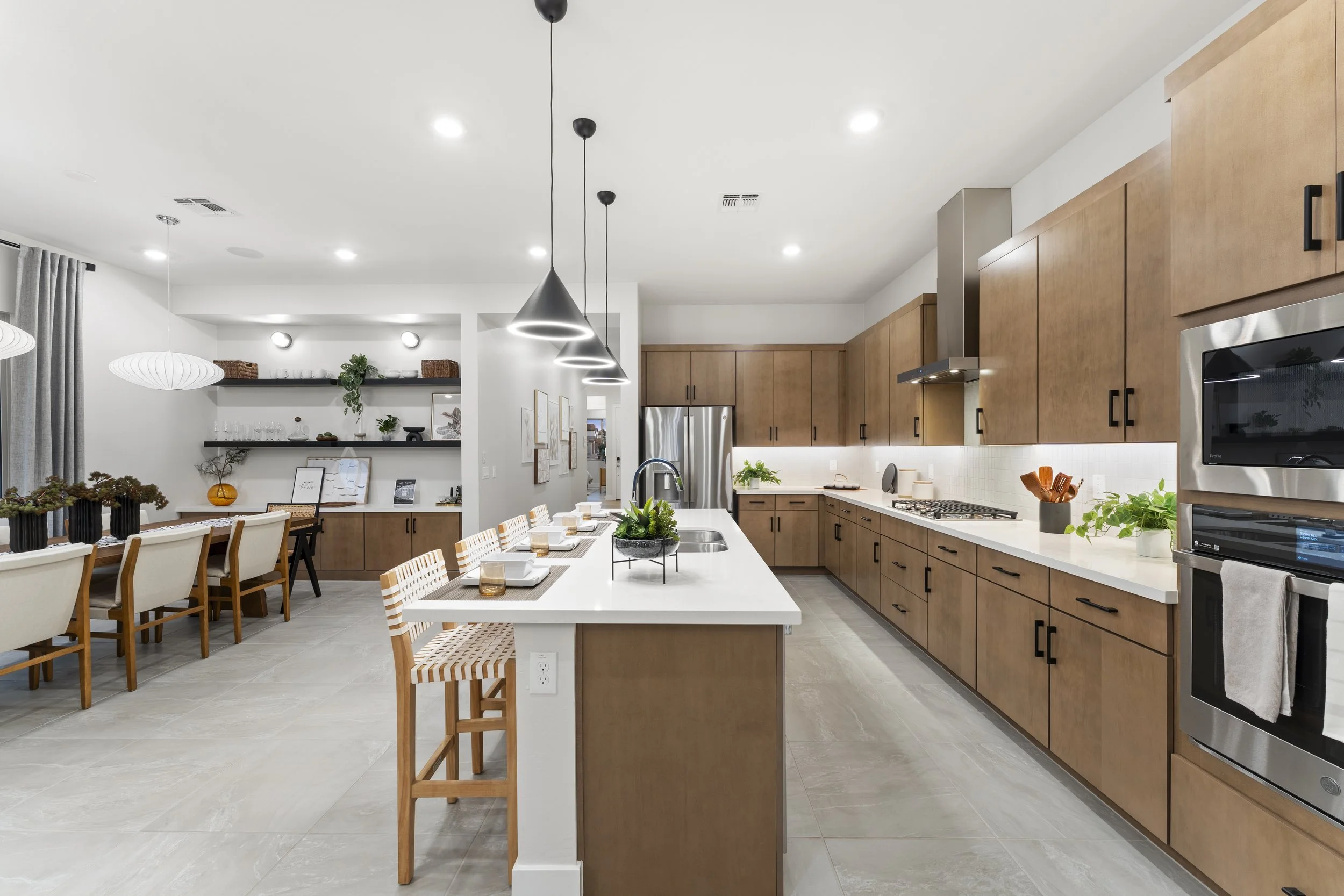 Modern kitchen with wooden cabinets, white countertops, stainless steel appliances, and black fixtures, with an island and adjacent dining area.