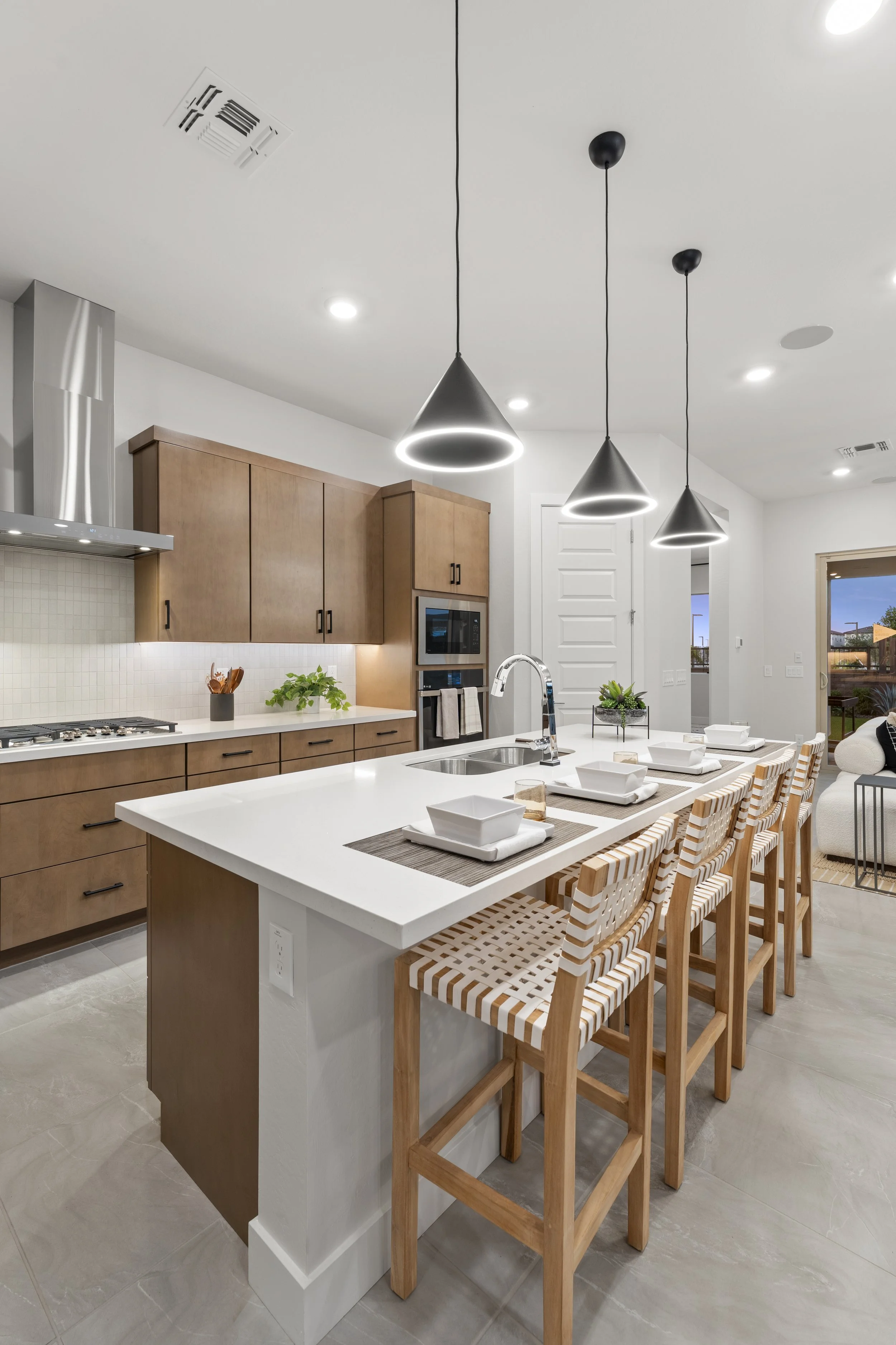 Modern kitchen with white island, wooden cabinets, black pendant lights, and dining setup with white dishes and striped chairs.