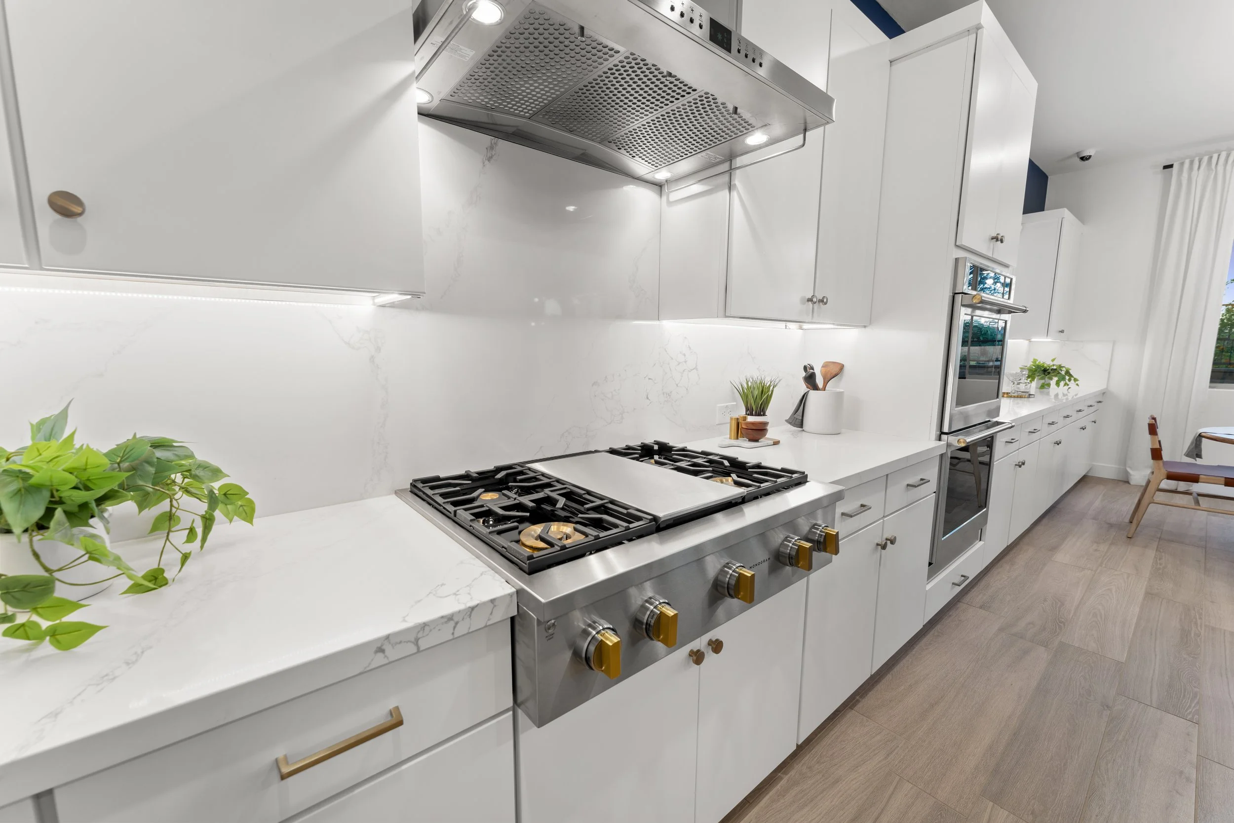 Modern kitchen with white cabinets, marble countertop, stainless steel gas stove, built-in oven, and minimal decor.