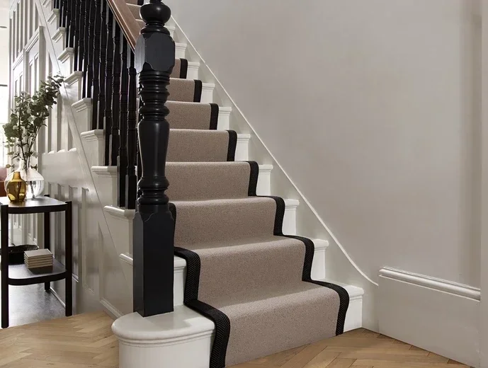 Interior view of a staircase with beige runner rug, black border, black banister, and white walls in a home.