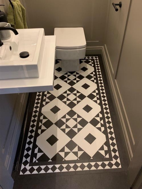 Bathroom with black and white patterned tile floor, white sink, and a modern toilet near a door.