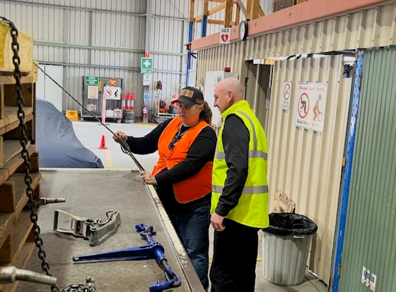 Two workers in safety vests inspecting equipment inside a warehouse or industrial facility.