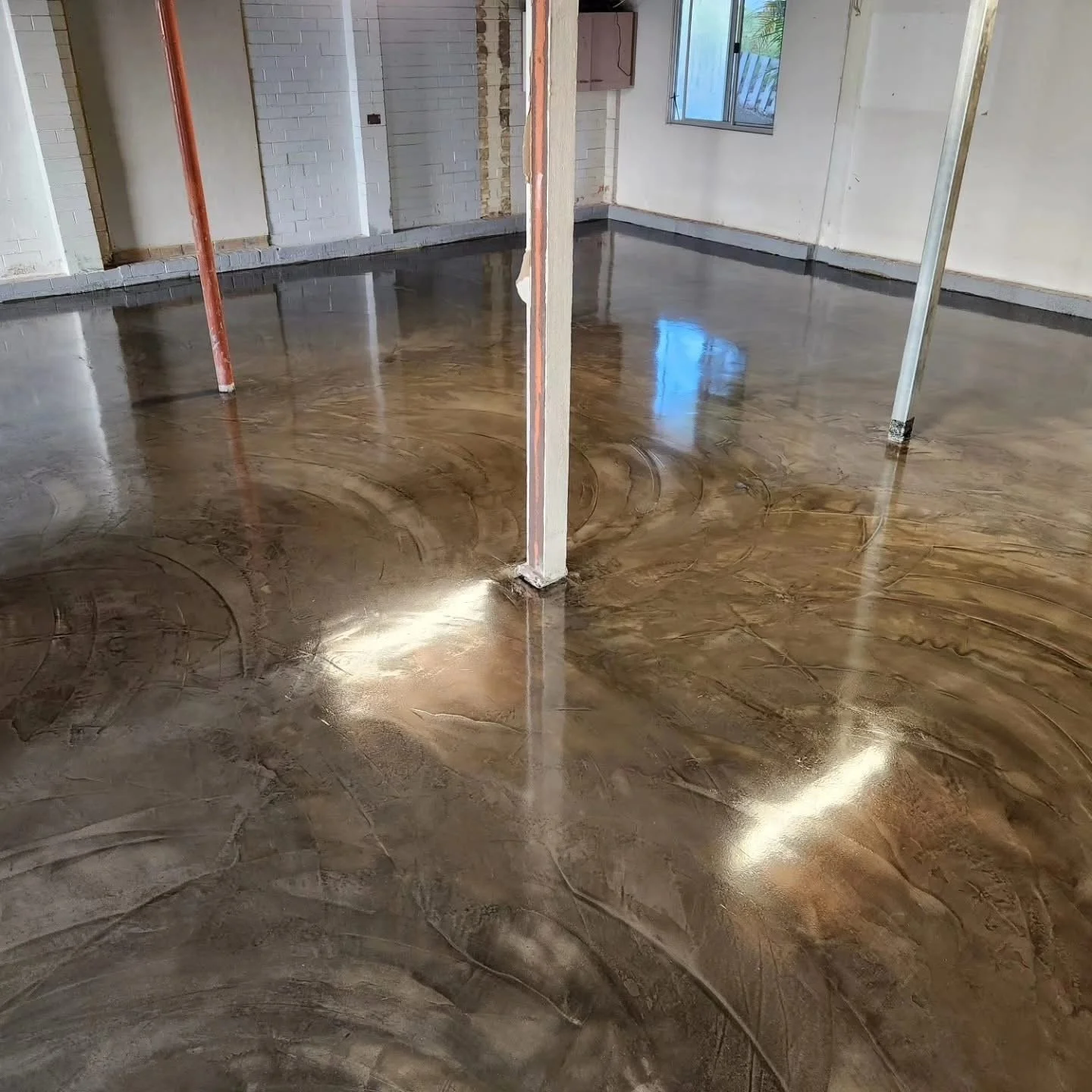 Interior of a building with a newly polished decorative concrete floor, featuring swirling marble-like patterns, with supporting columns and a window visible in the background.
