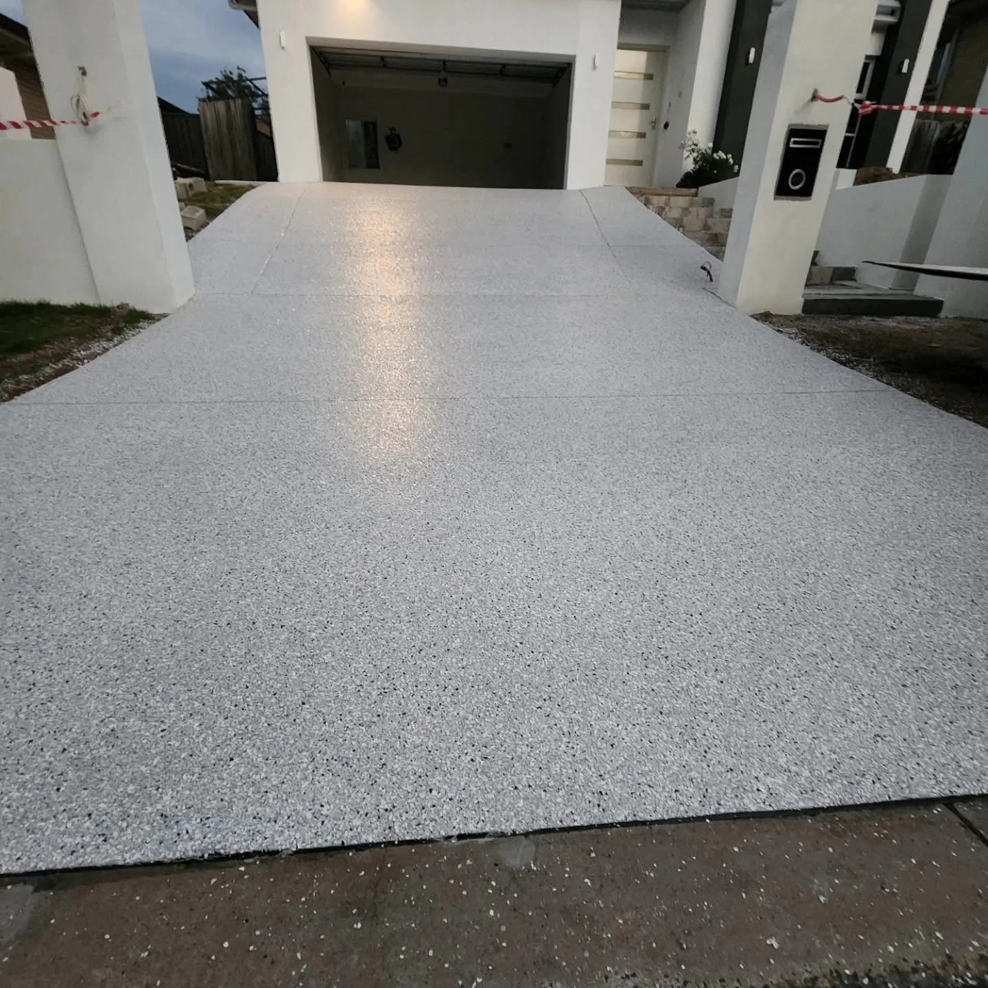 A freshly laid, textured, gray concrete driveway leading up to a modern house with white walls and a garage entrance.