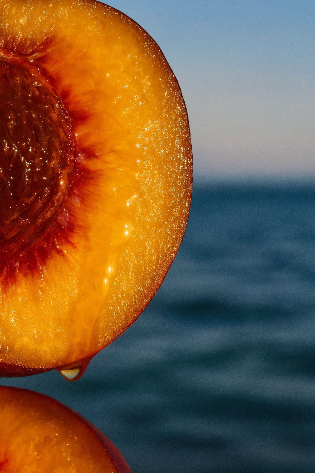 Close-up of a sliced peach with a water droplet, against a blurred blue background.