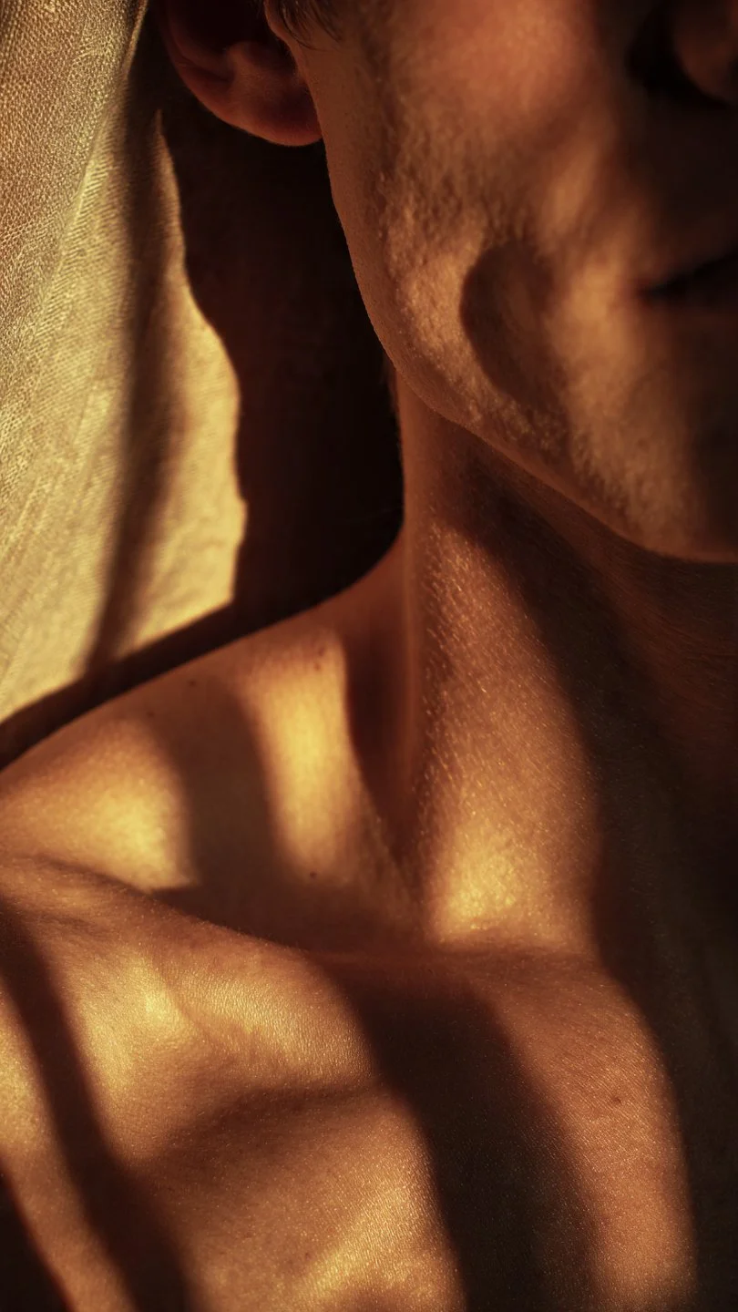 Close-up of a person's neck, shoulder, and part of the face with warm, soft lighting creating shadows on the skin.