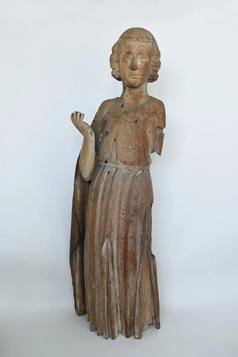 Eine antike Holzfigur einer lächelnden Frau mit kurzen, lockigen Haaren, die einen Arm angehoben hat, vor einem weißen Hintergrund.