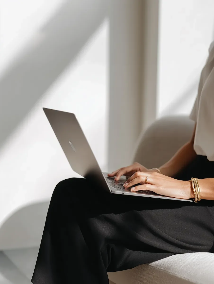 Female sitting in window light with laptop in lap.