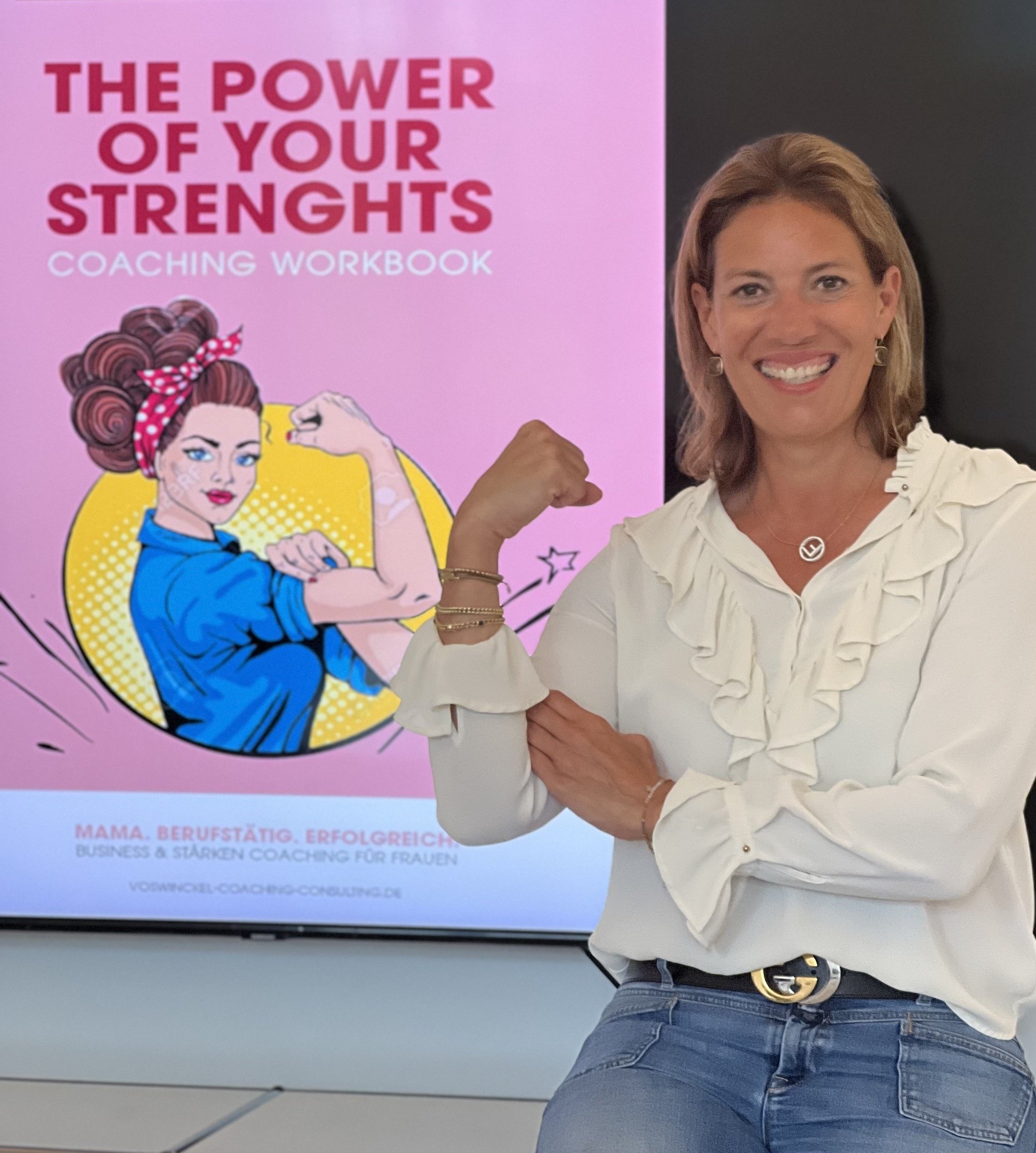 Eine Frau posiert vor einem Bildschirm mit einem feministischem Motiv. Sie trägt ein weißes Hemd und zeigt ihren Bizeps, um Stärke zu symbolisieren.