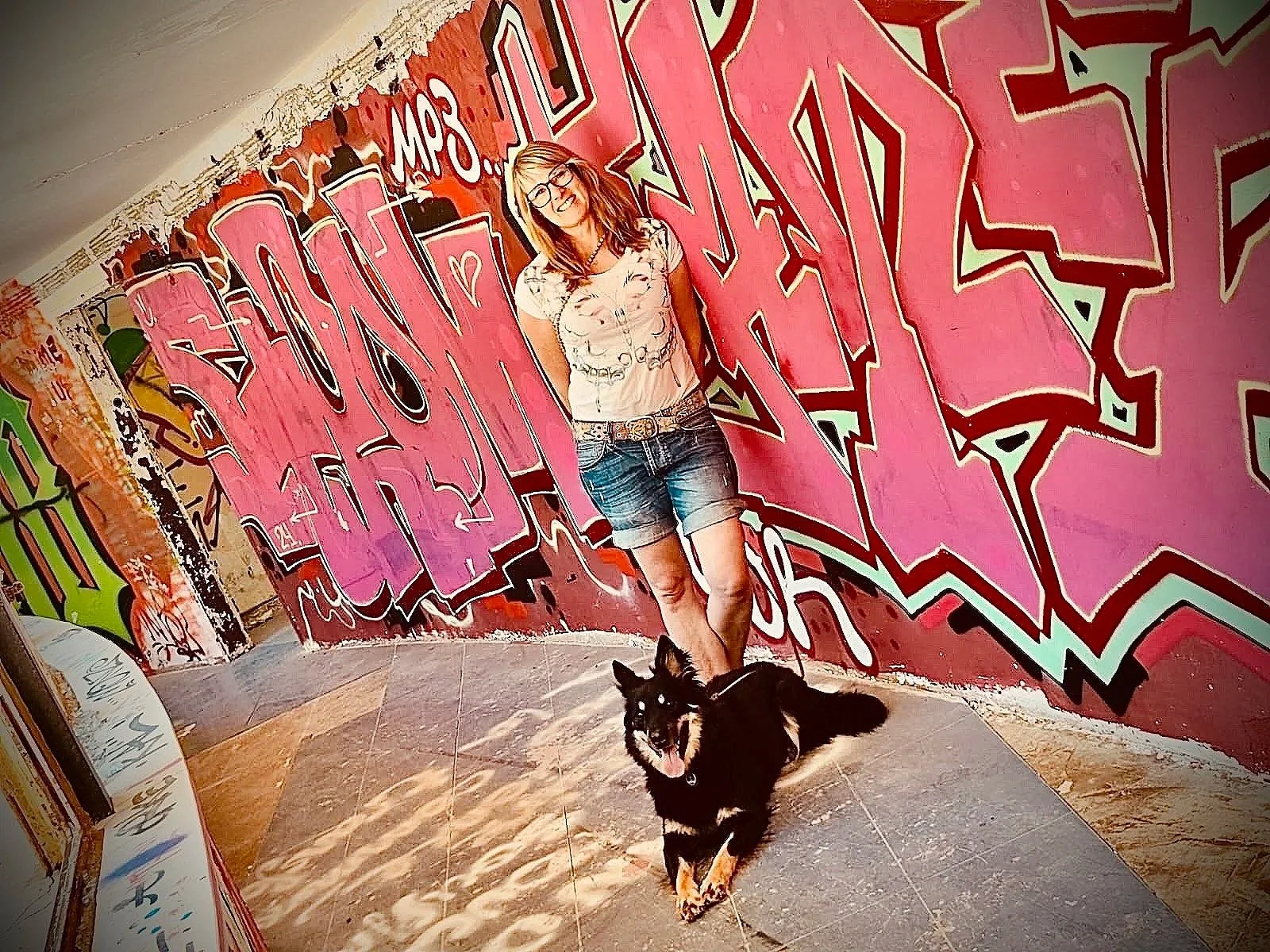 Frau mit Hund vor einem bunten Graffiti an der Wand.