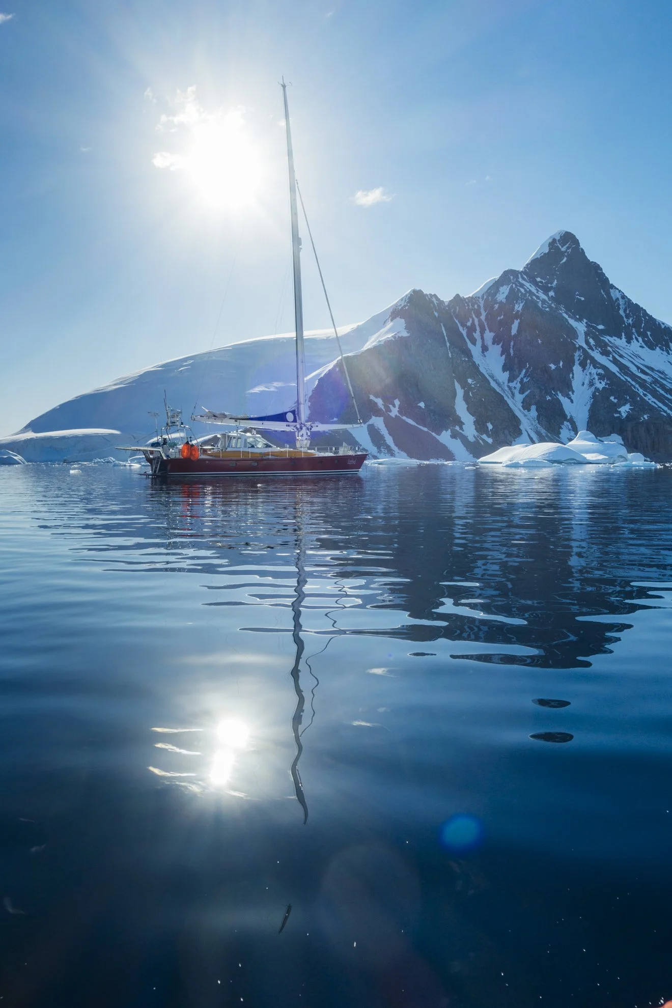 A boat floating on calm water with snow-covered mountains and glaciers in the background under a bright sun.