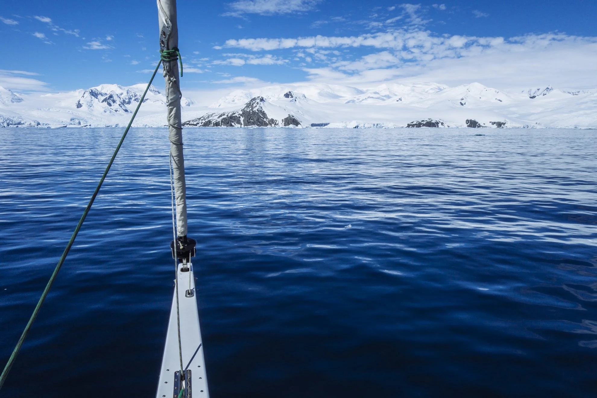 View from a boat in icy waters with snow-covered mountains in the background and a partly cloudy sky.