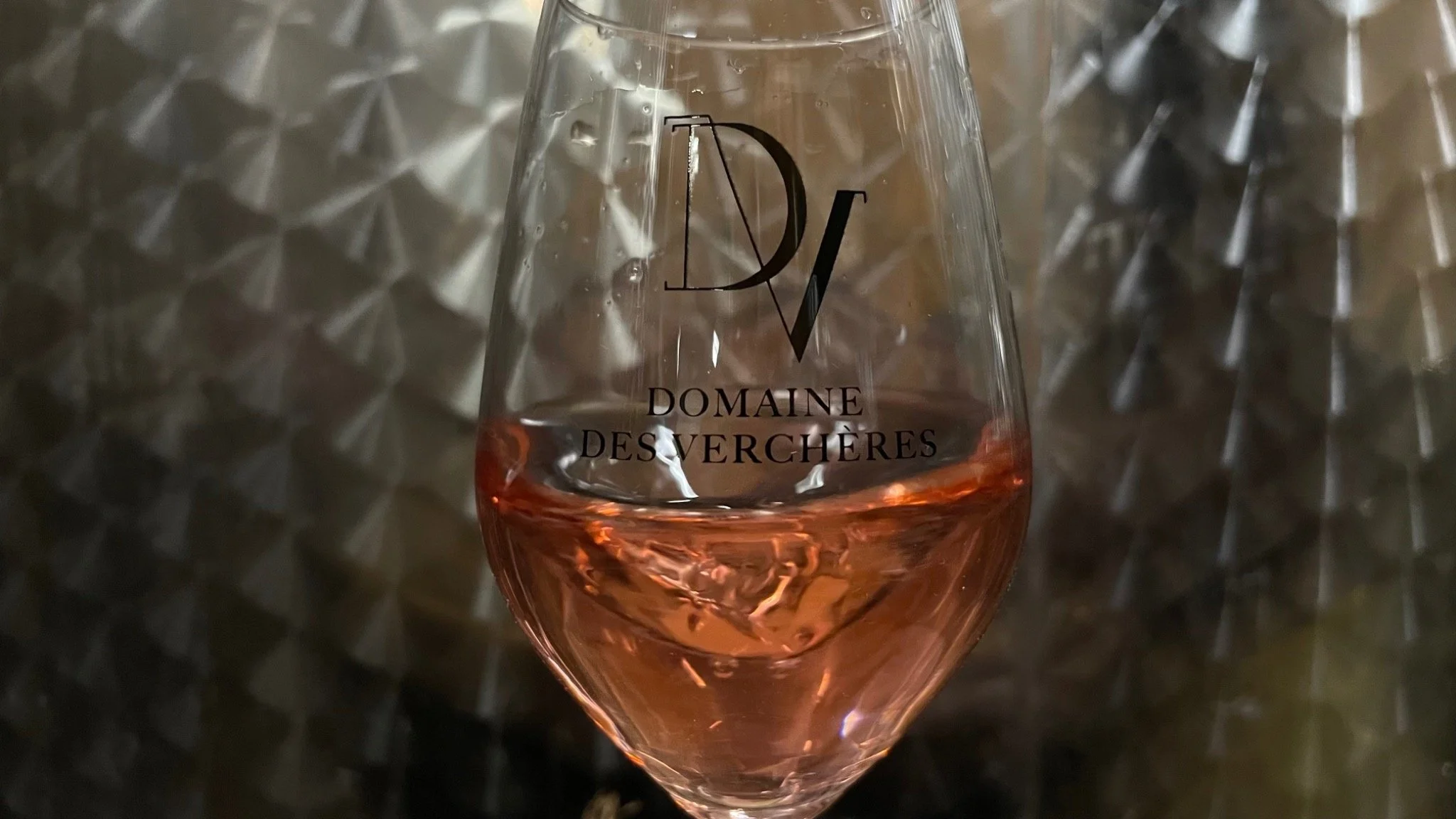 Verre de vin rosé avec le logo 'Domaine des Verchères' en gros caractères noir, posé sur une surface métallique réfléchissante.