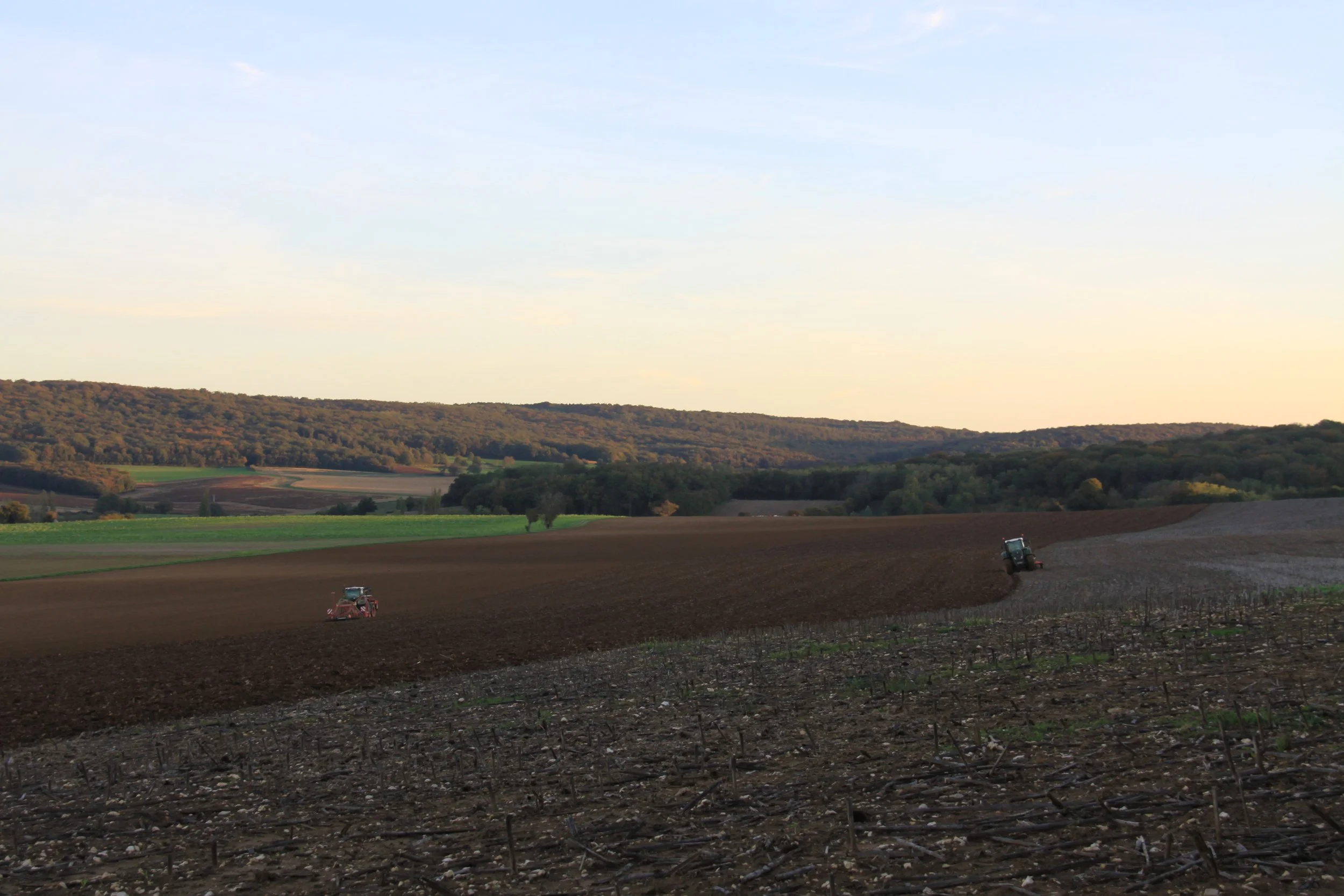 Champs agricoles avec deux tracteurs en train de travailler la terre pour semer du blé.