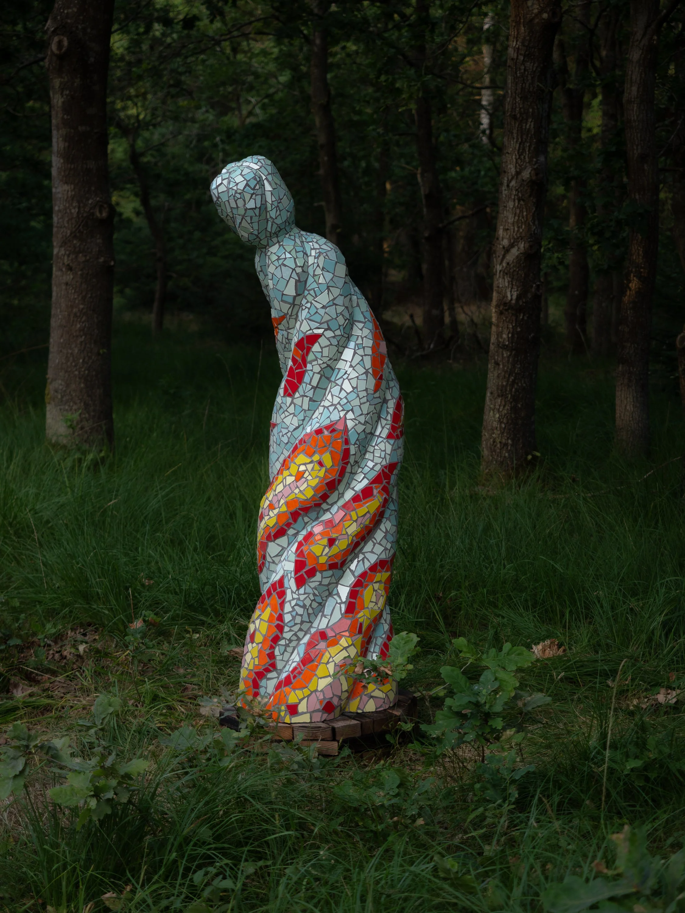 A mosaic sculpture standing among trees and grass.