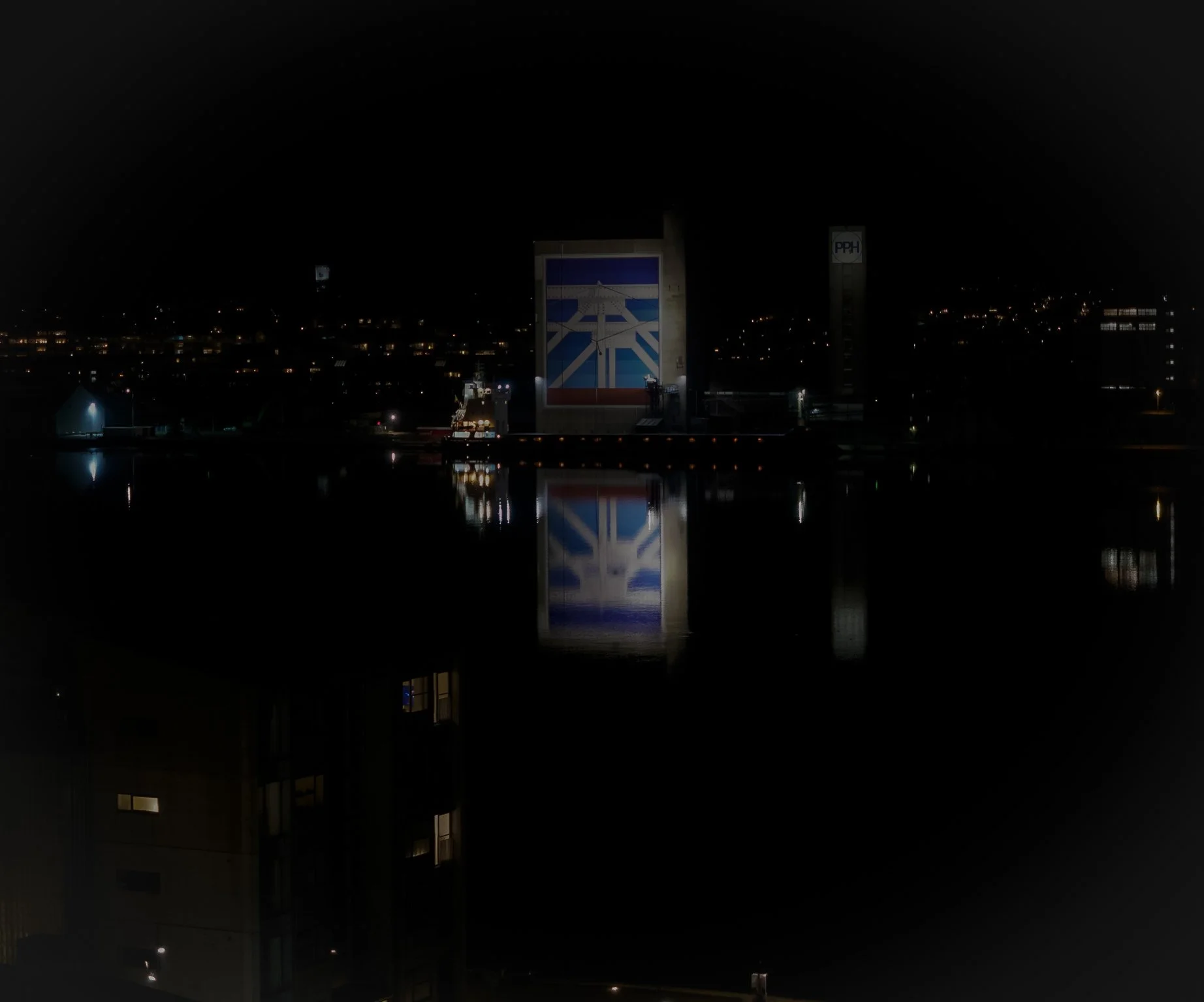Illuminated industrial building reflected in water at night.