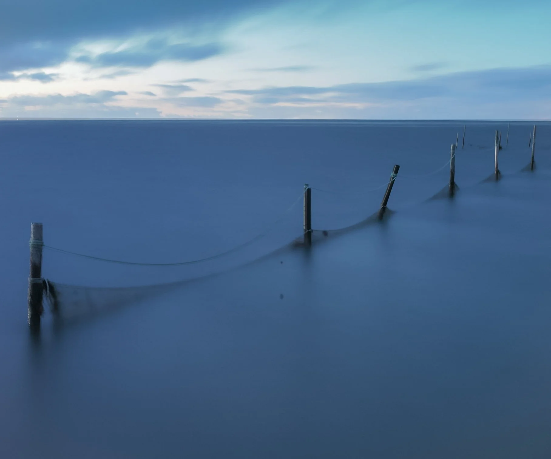 Wooden posts connected by rope extending into calm water.