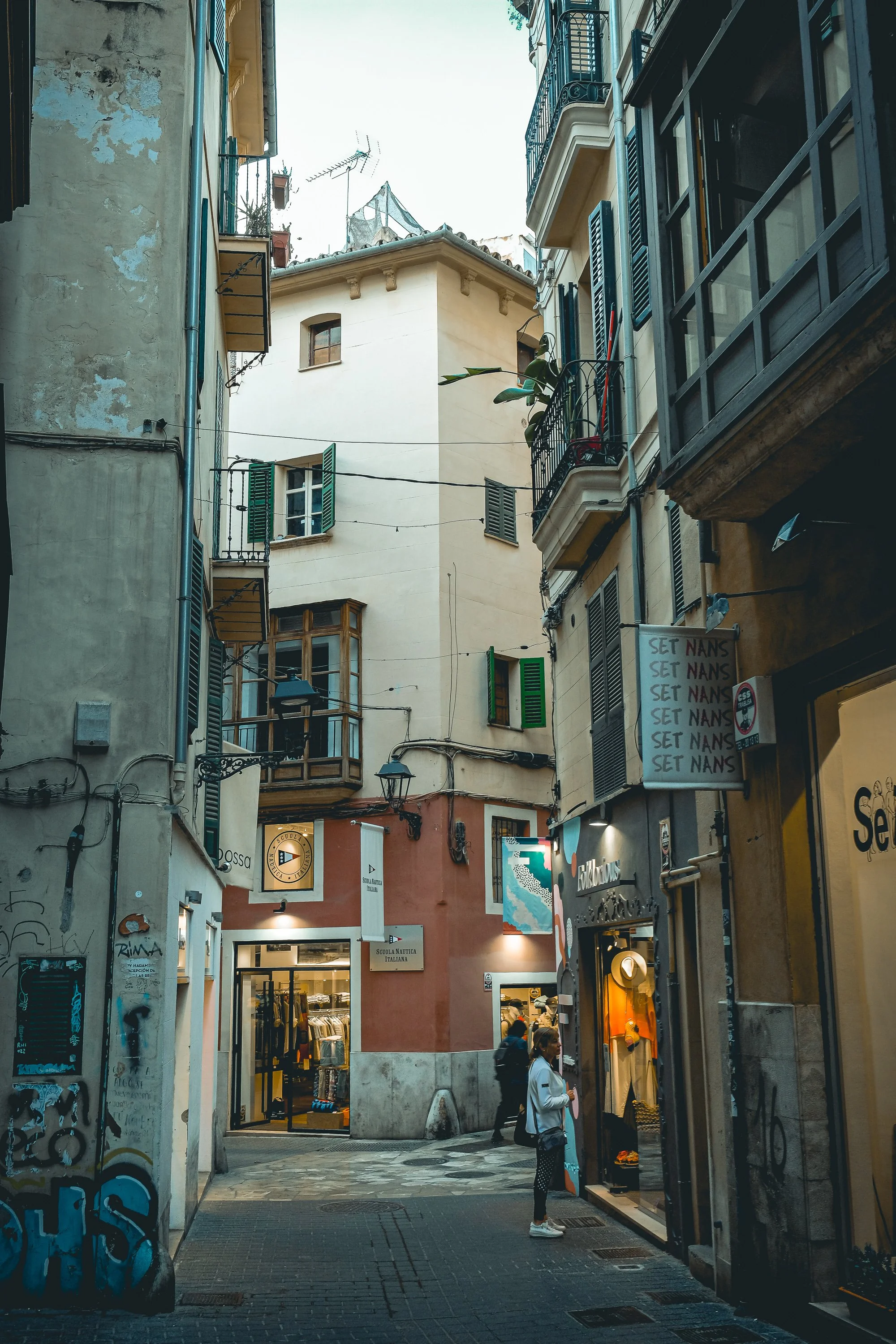 Narrow street between buildings with signs and balconies.