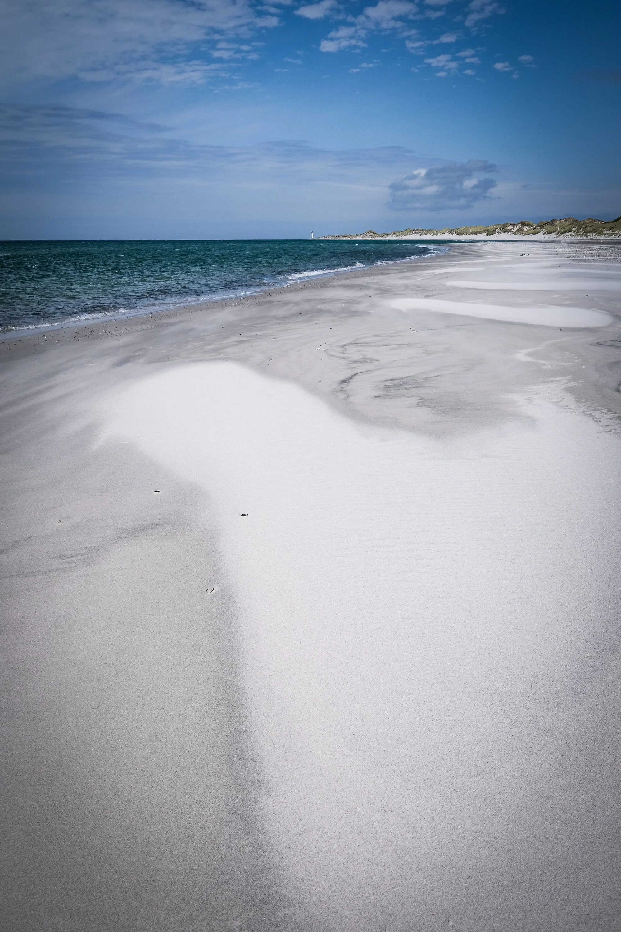 Sandy beach and sea under a cloudy sky.