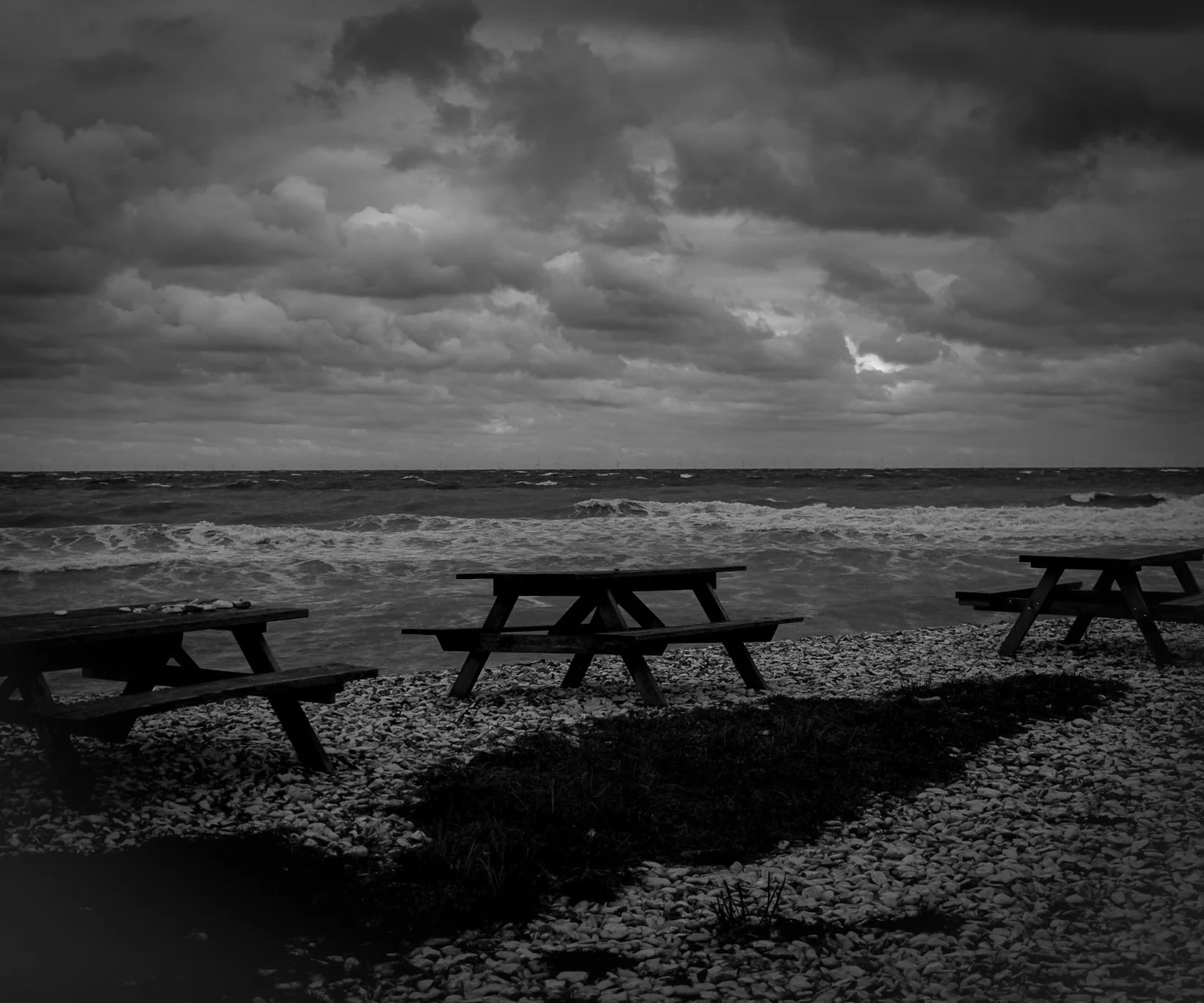 Black-and-white photograph of empty picnic tables by the sea.