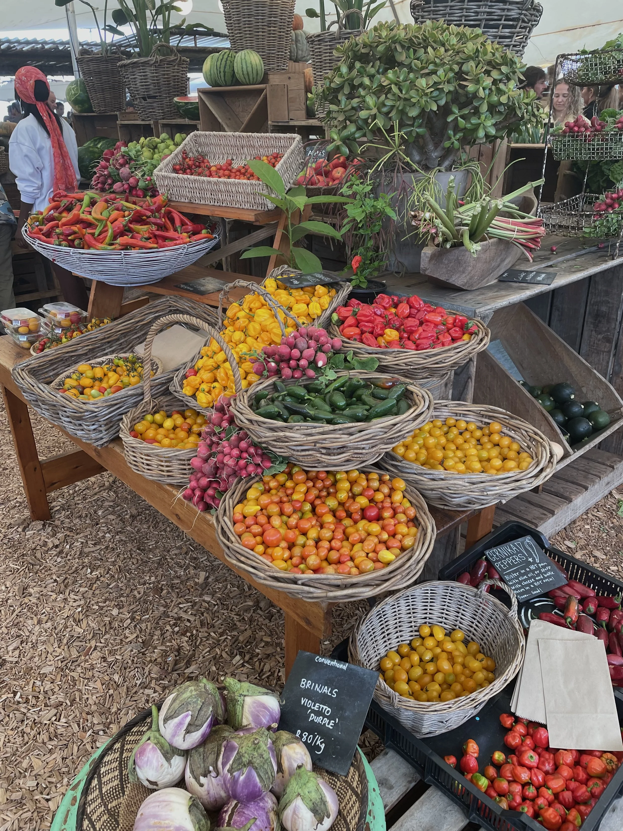 Basket of cherry tomatoes of various colors in a market stall with other vegetables and plants around.