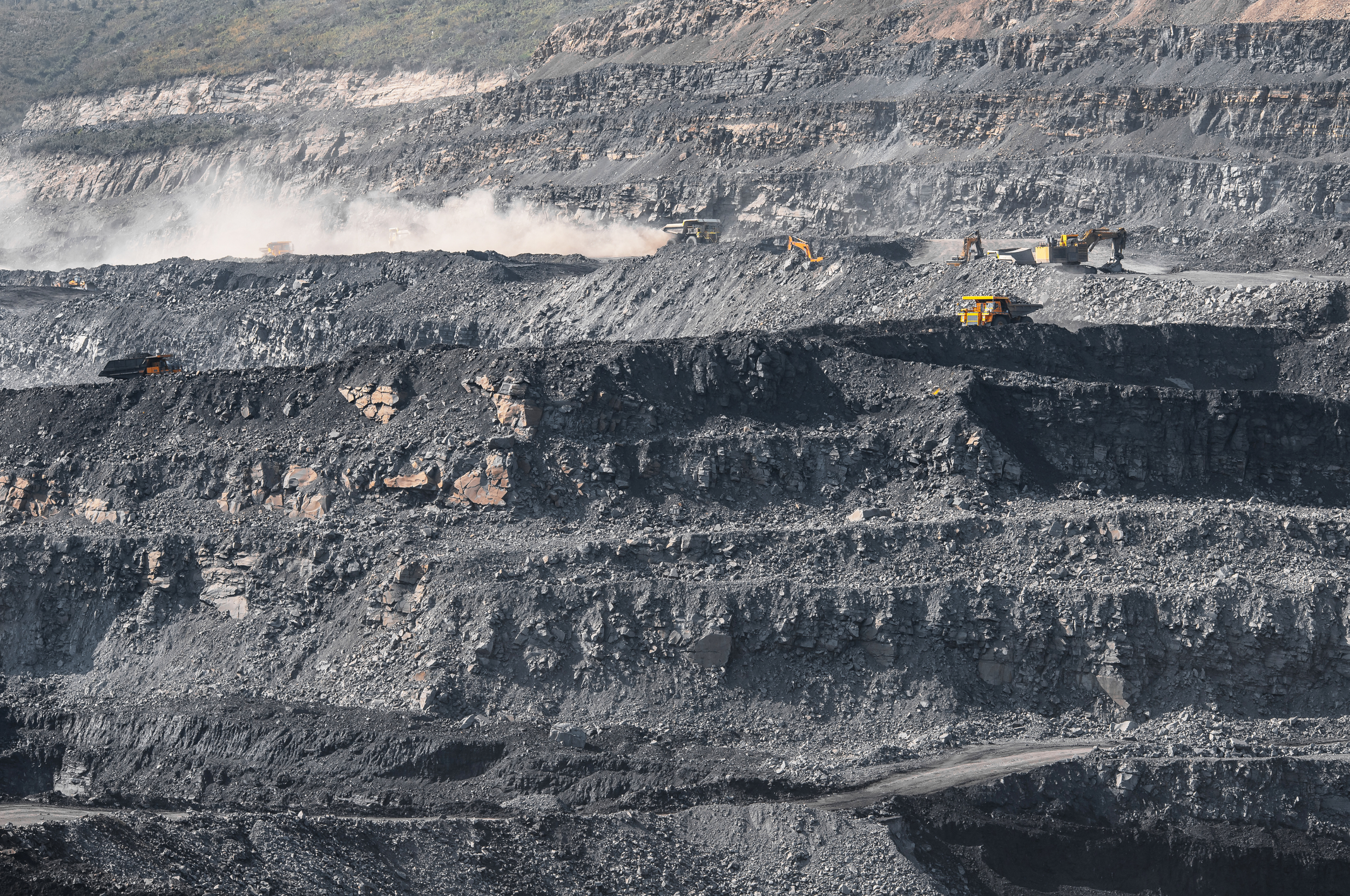 Multiple excavators working in an open-pit coal mine, digging and moving large amounts of earth and rocks.