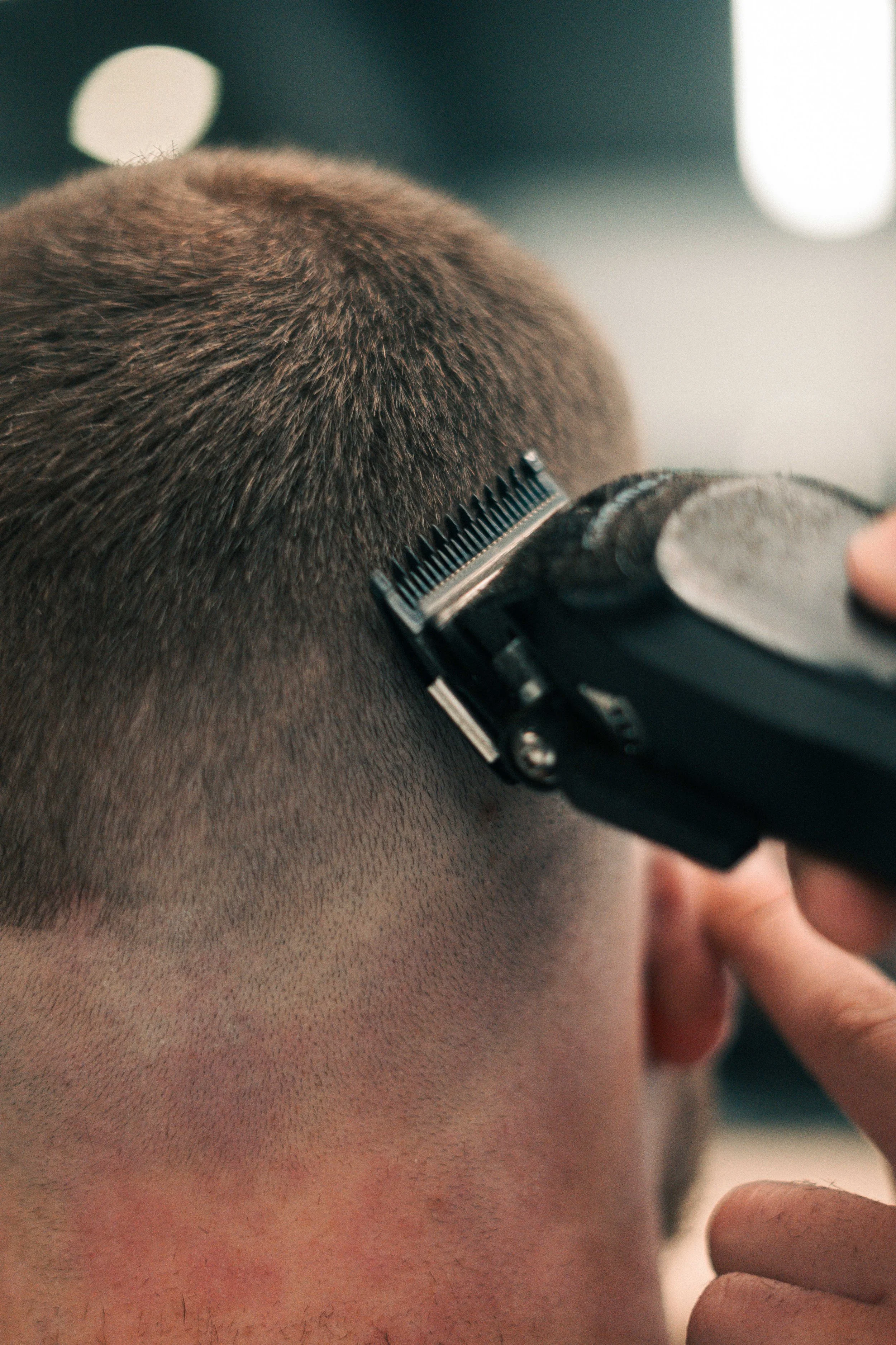 Close-up of a person getting a haircut with a clipper trimming the back of their head.