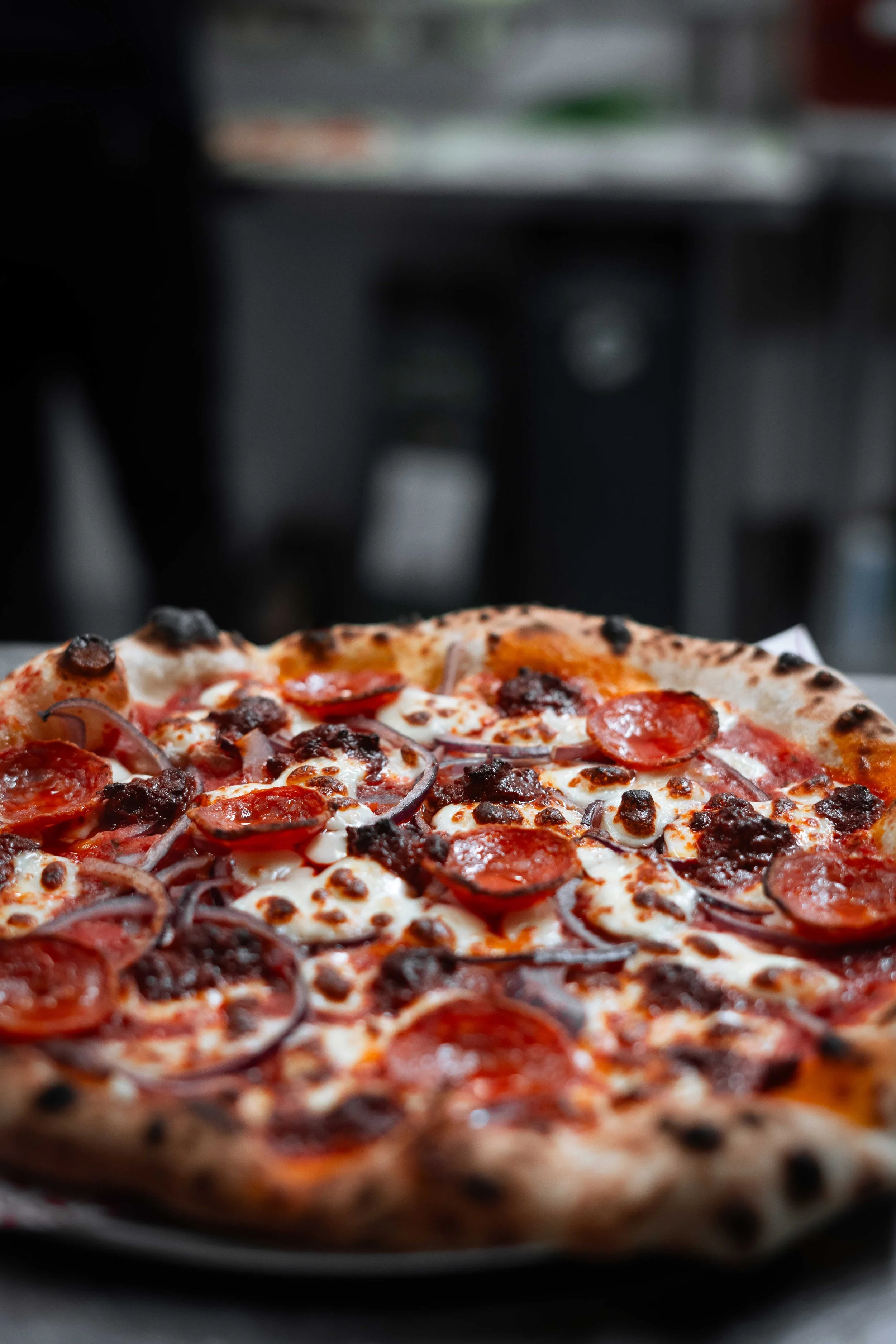 Close-up of a pepperoni pizza with onions and crumbled sausage on a pizza table.
