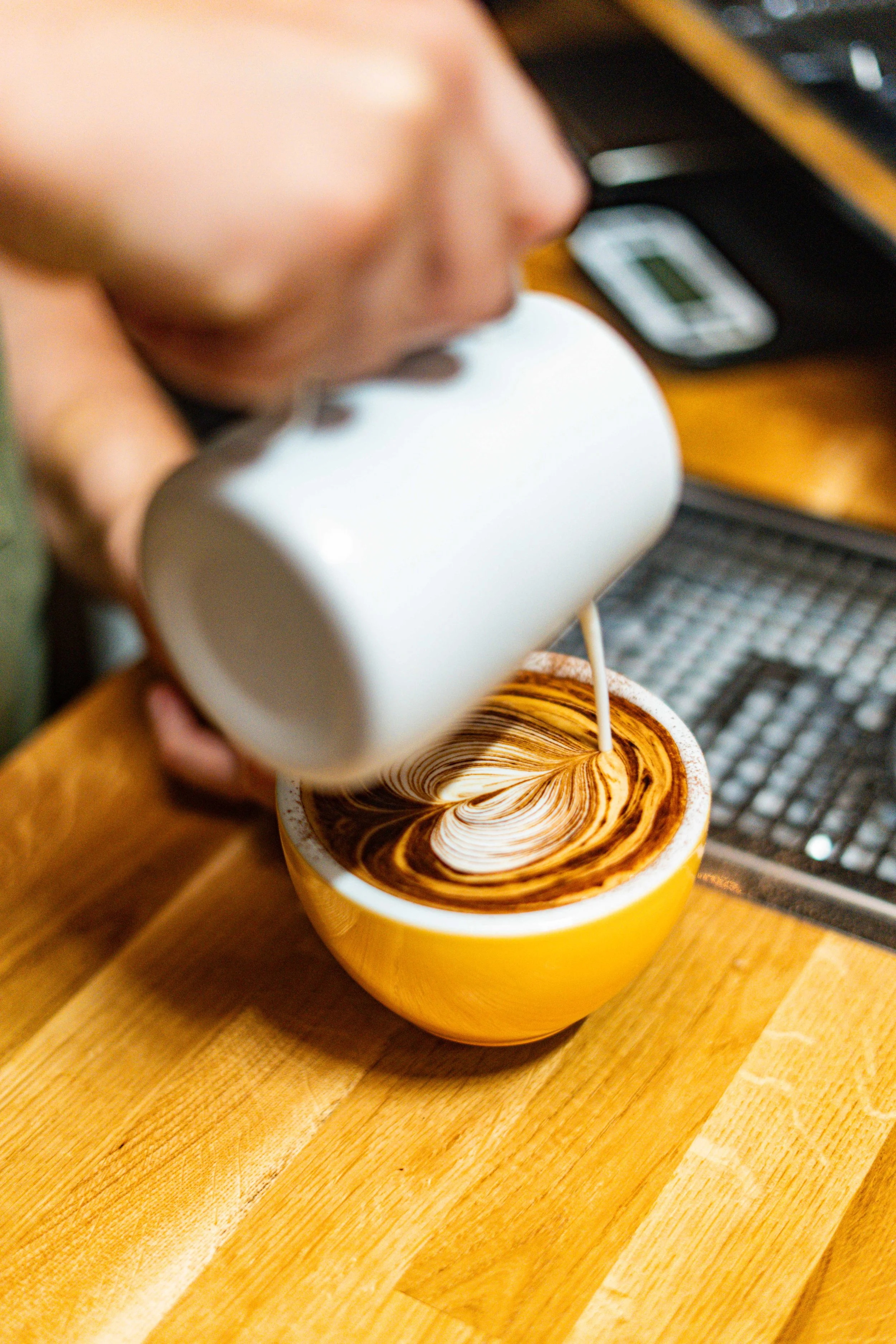 A person pouring milk into a cup of coffee to create a latte art pattern.