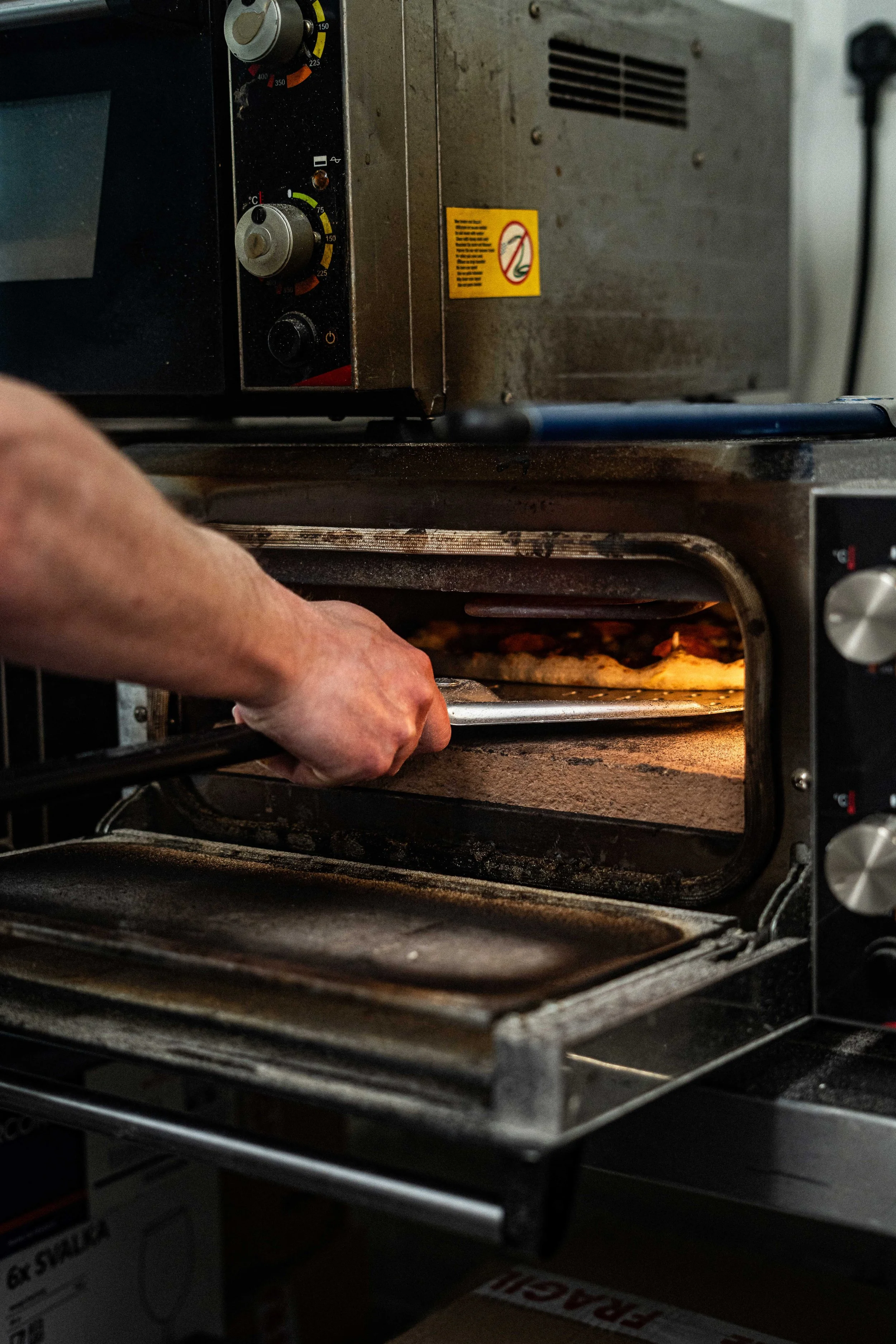 Person placing food into a commercial oven, with the oven door open and oven racks visible.