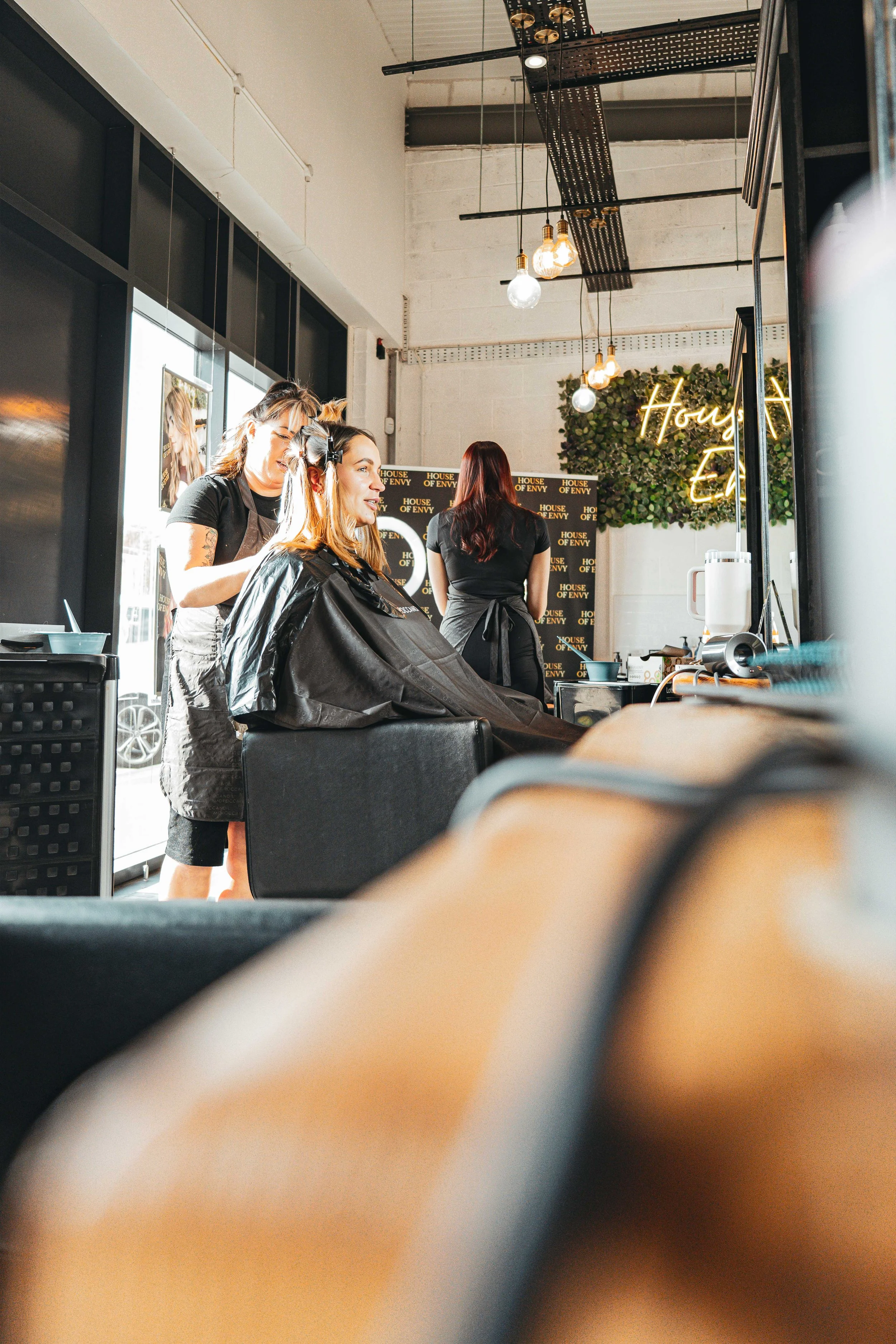 Women at a hair salon getting haircuts, with a stylist cutting one woman's hair and multiple women waiting or working in the background.