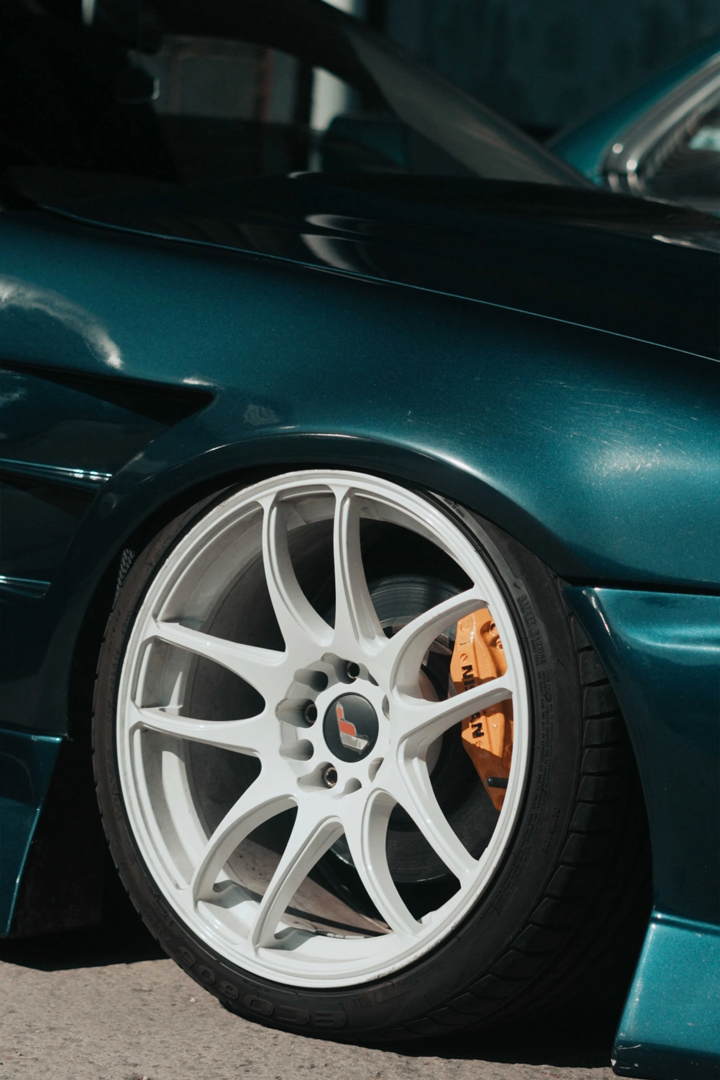 Close-up of a sports car with a green body, white rimmed wheel, and orange brake caliper.