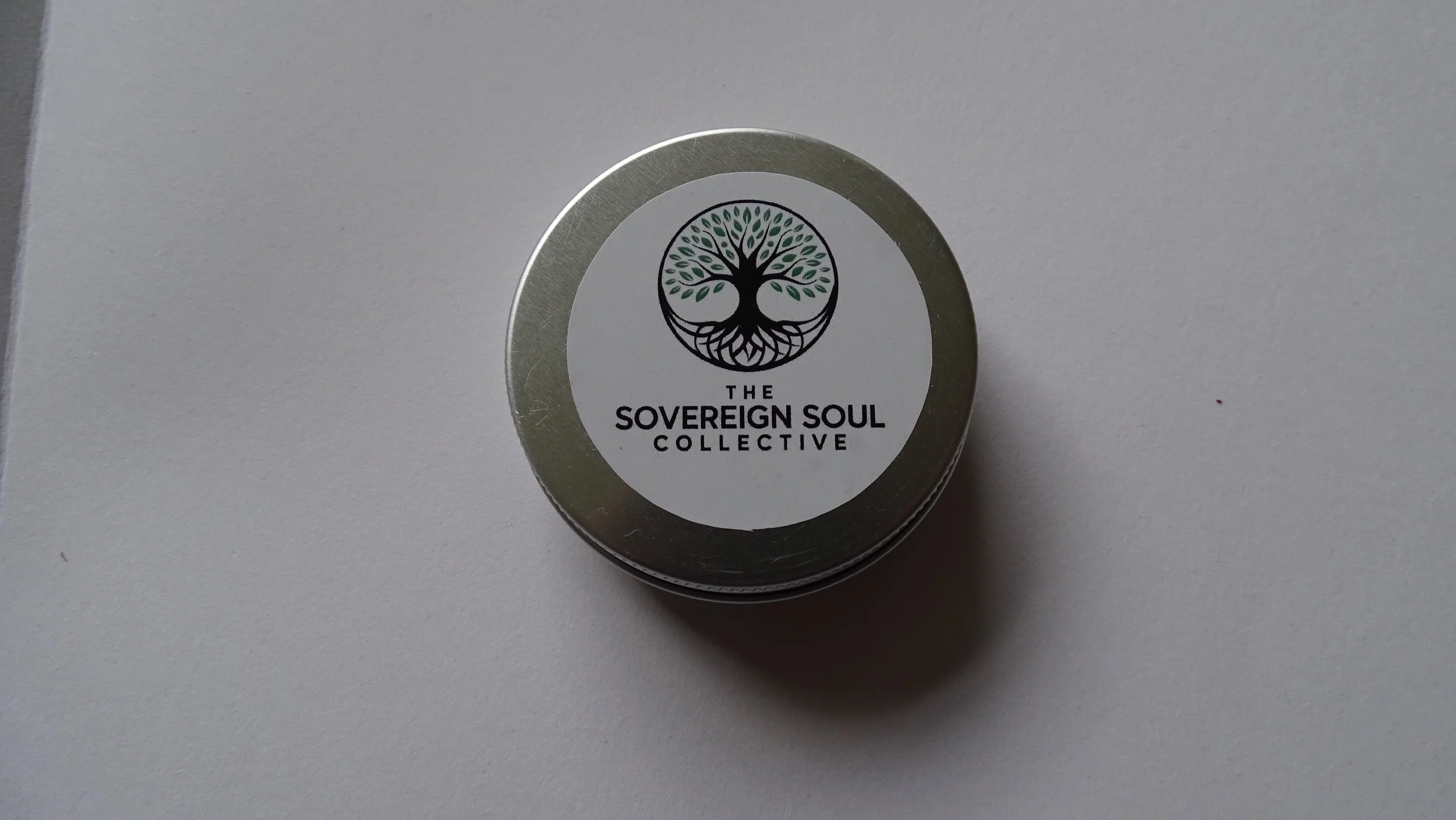 A round metal container with a label that has a black tree logo and the text 'The Sovereign Soul Collective' on a white background.