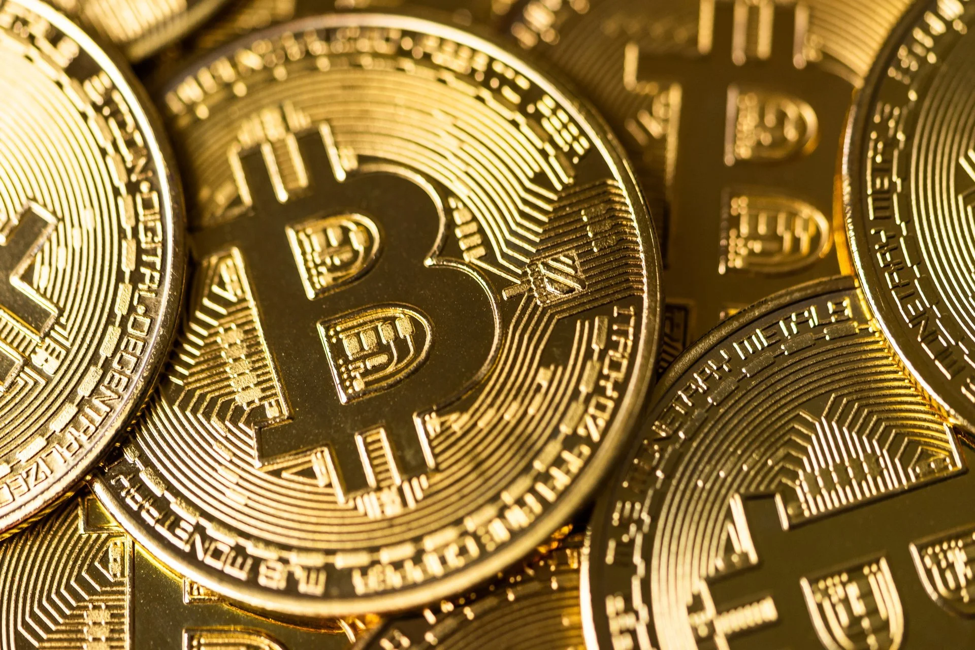 Close-up of several gold-colored Bitcoin coins, showing the Bitcoin symbol and intricate circuit-like design.