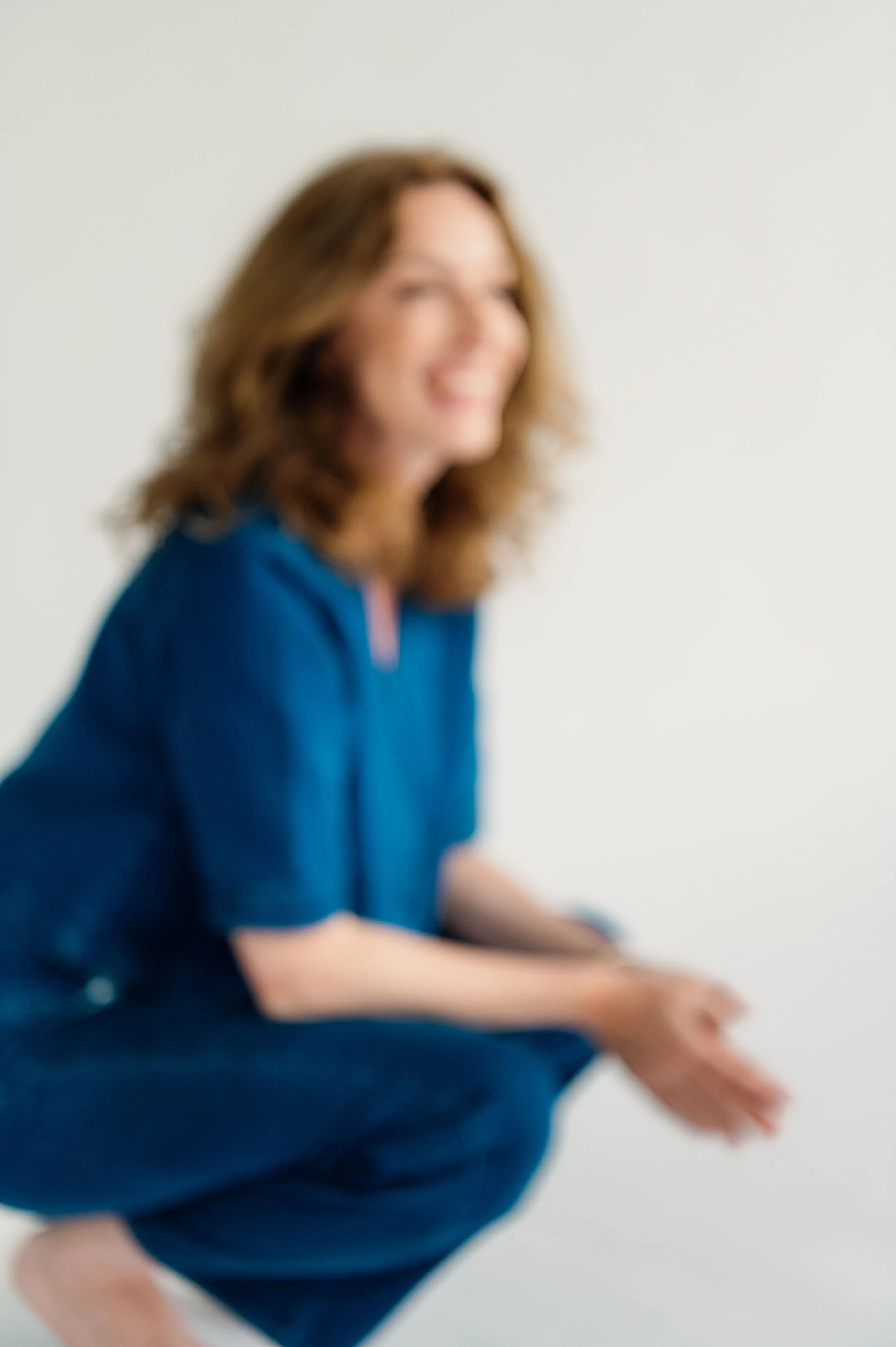 Een lachende vrouw in een blauwe outfit, die in een rustgevende witte ruimte zit.