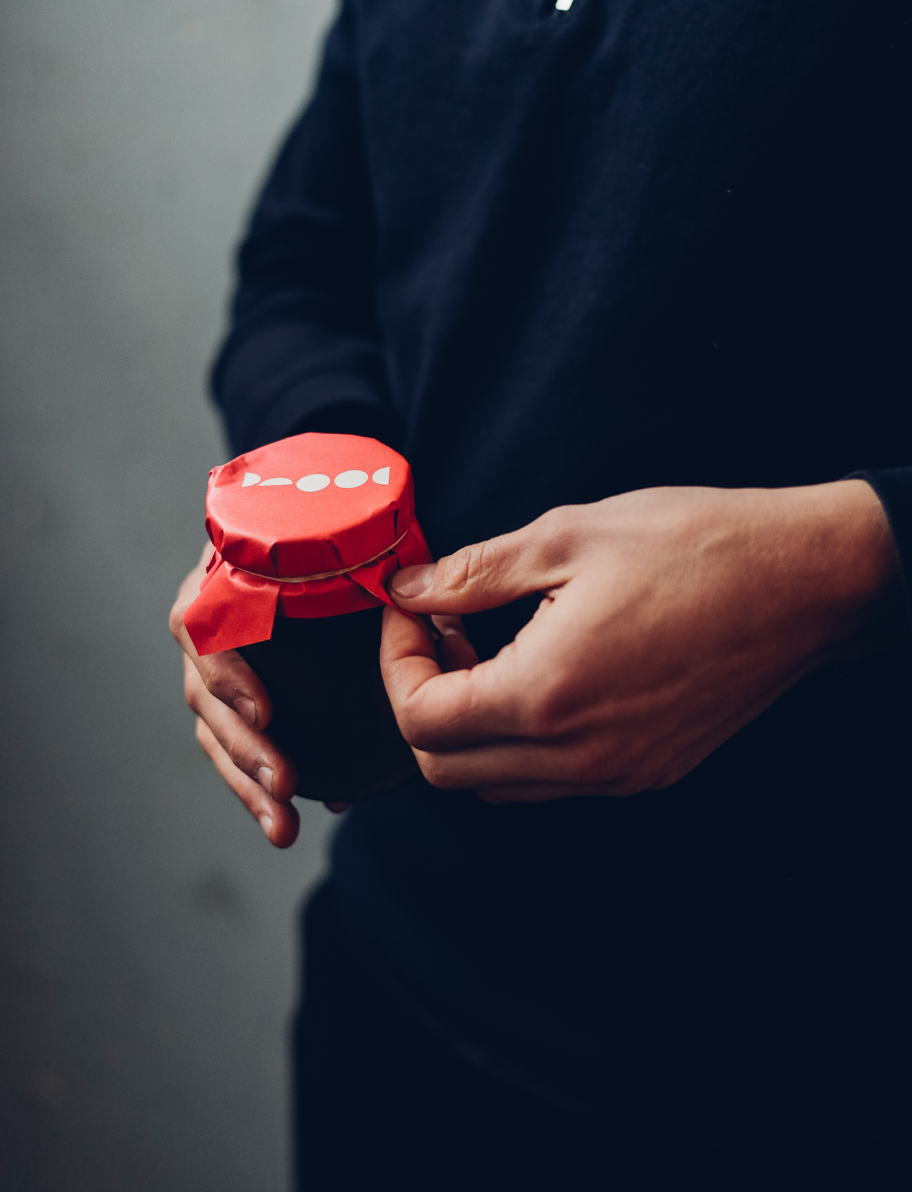 Person holding a jar of broth with a red paper cover tied with a string.