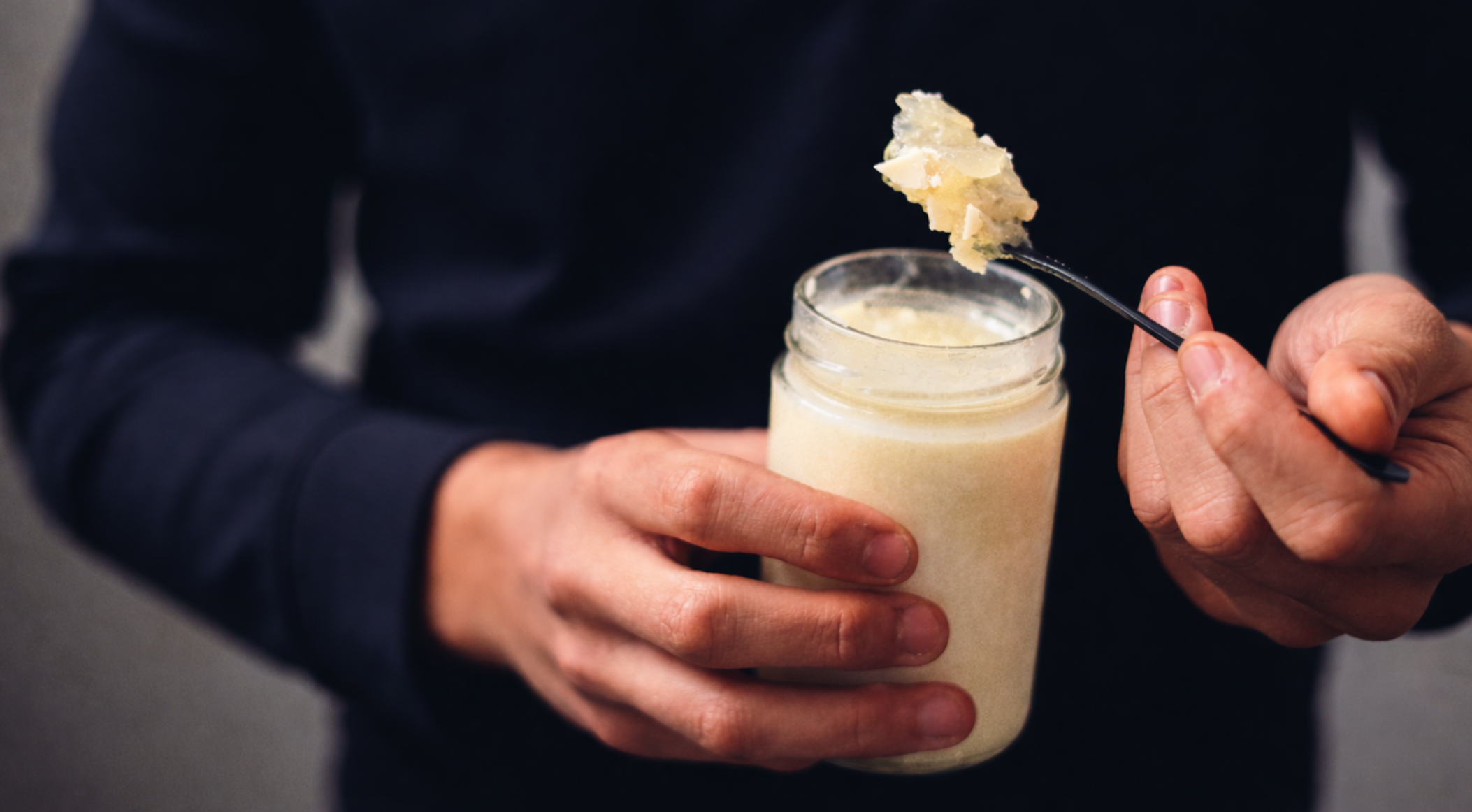Person holding a glass jar with chicken bone broth with a spoonful of gel.