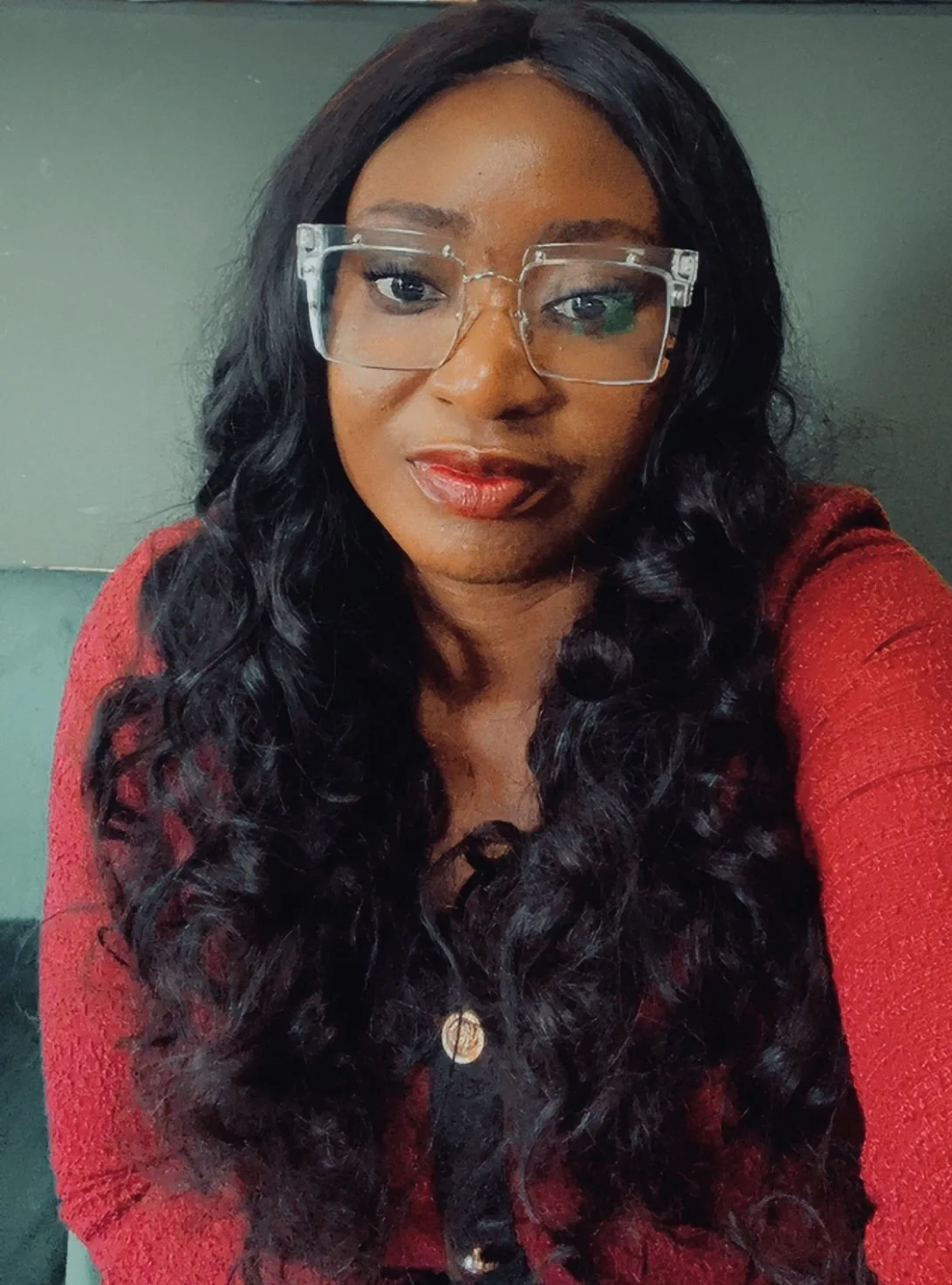 A woman with long, curly black hair wearing clear glasses and a red top taking a selfie.