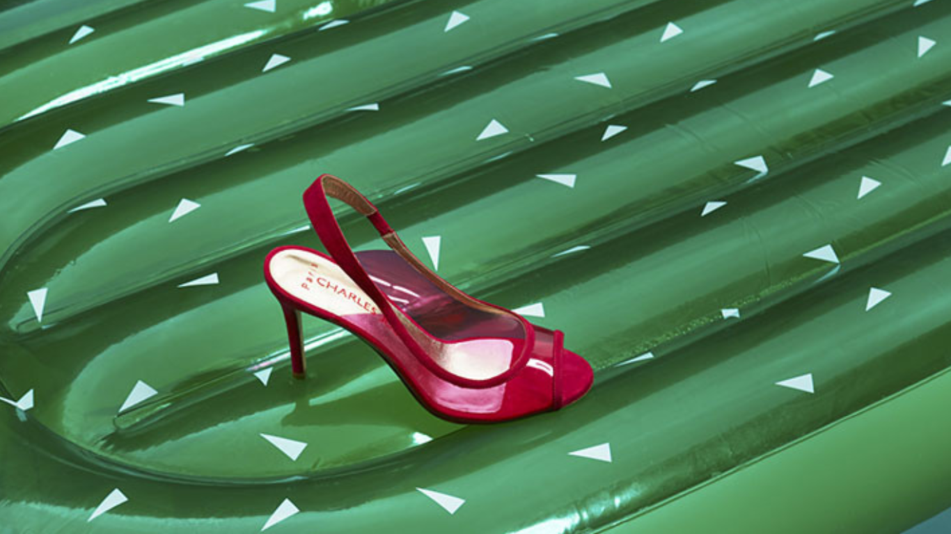 Une sandale rouge à talon sur une surface verte avec des motifs en forme de flèches blanches.