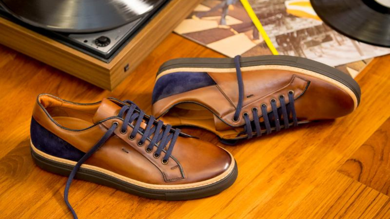 Une paire de chaussures en cuir marron avec des détails en daim noir, posée sur une table en bois, avec un tourne-disque au fond.