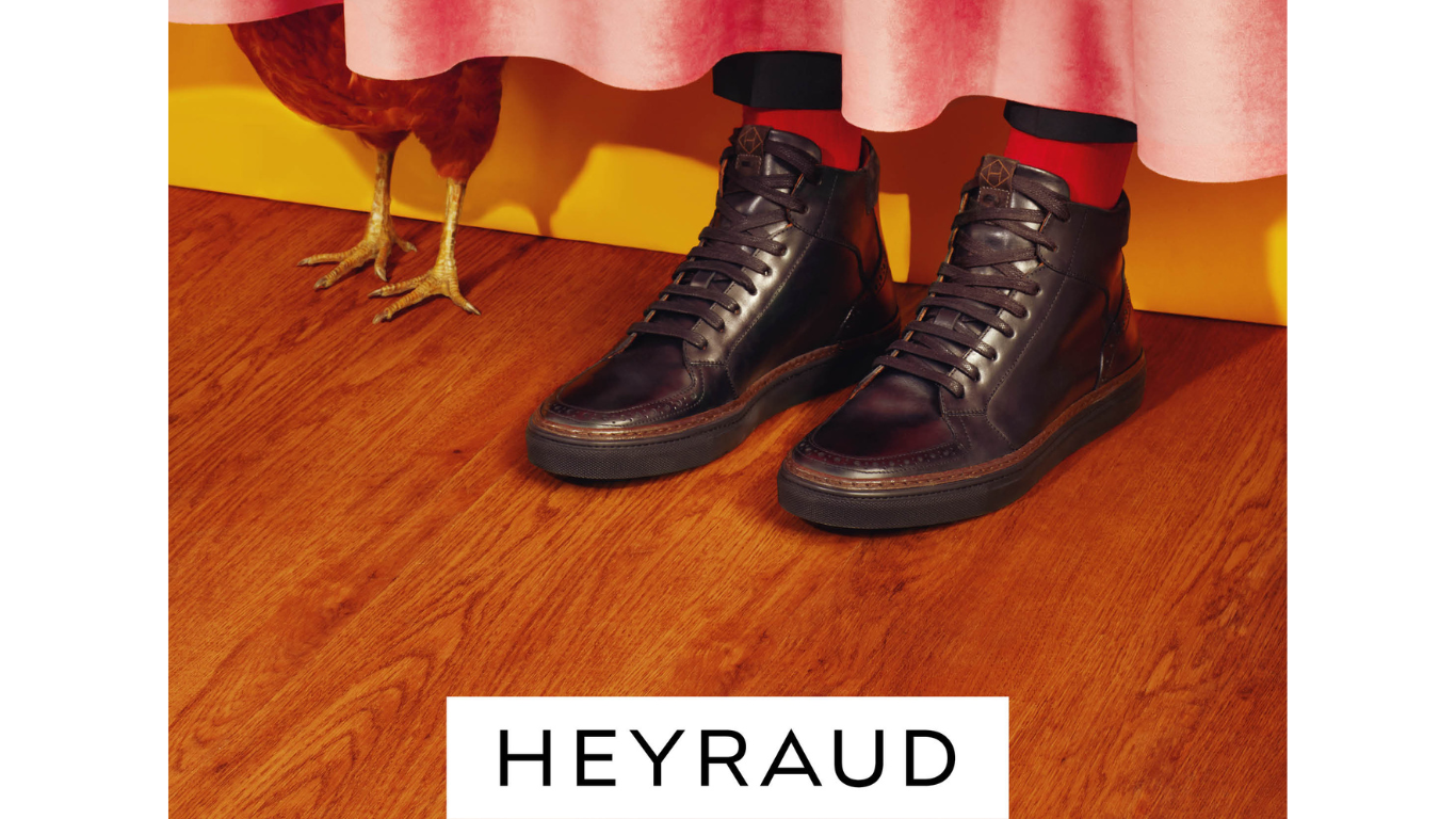 Chaussures noires en cuir, portée par une personne sous une jupe rose, avec un poulet à côté sur un plancher en bois