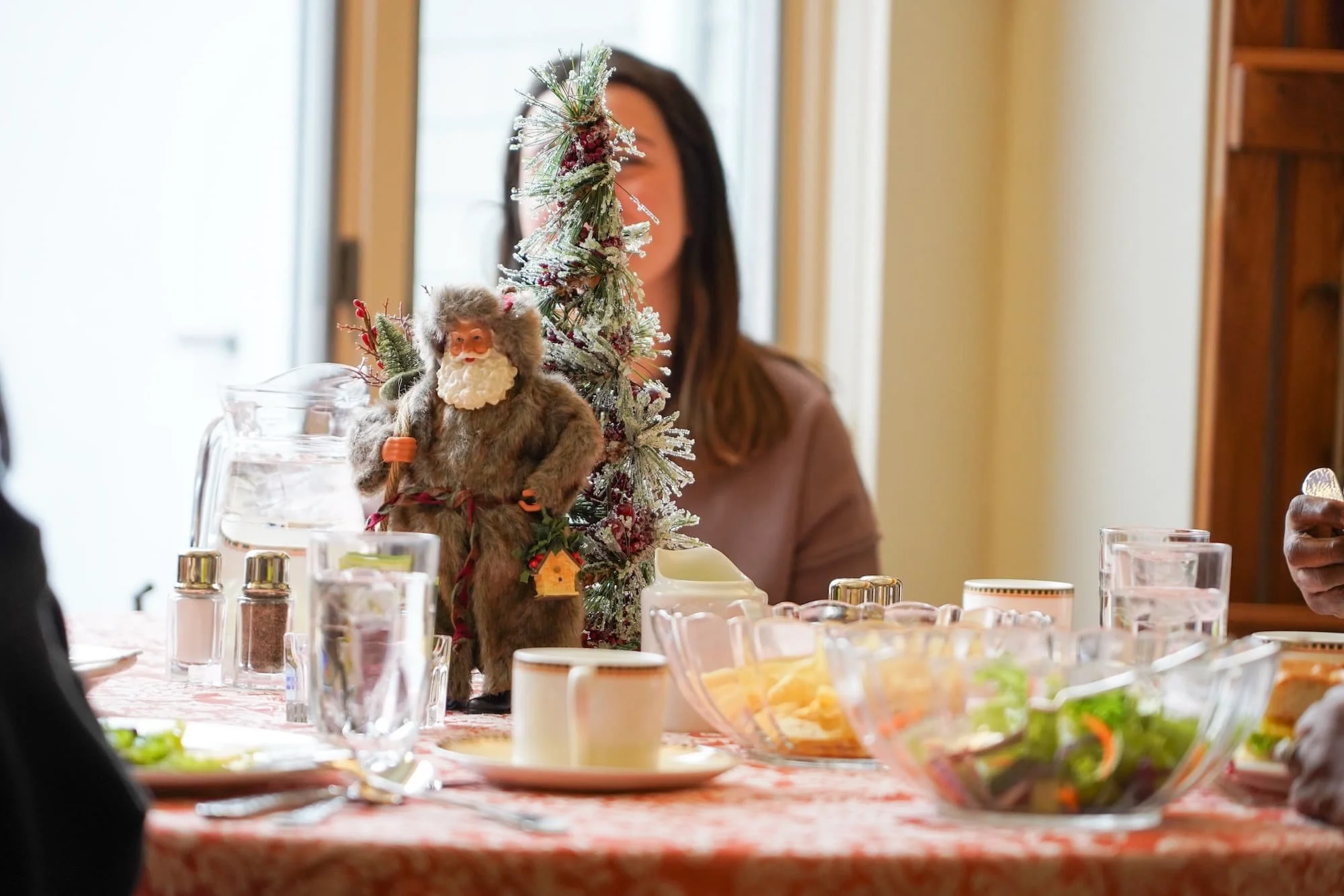 A decorated dining table with a small Christmas tree, a Santa Claus figure, and holiday-themed decorations, set for a meal with glasses, bowls, and plates in Arnold Hall dining room.