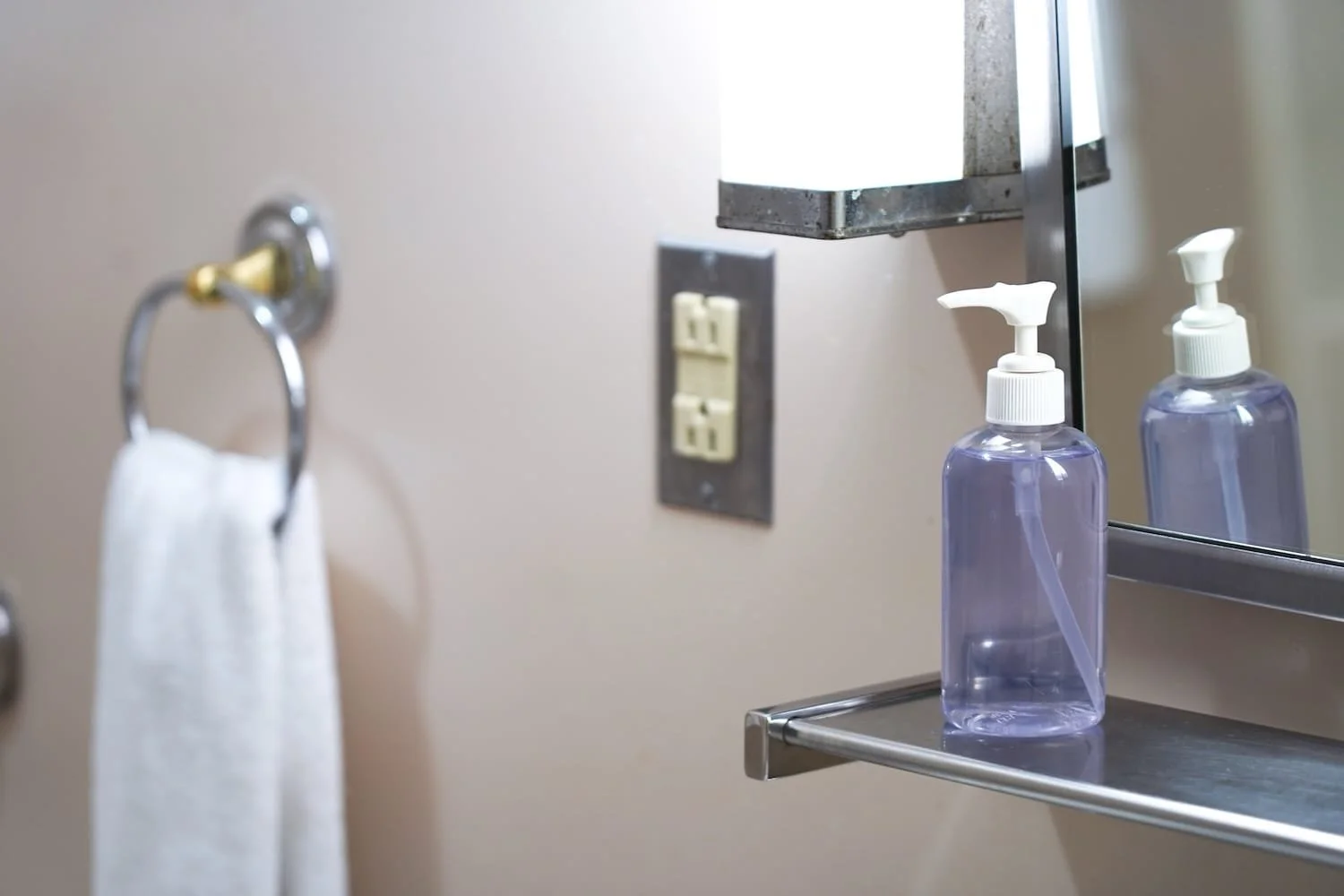 A bathroom countertop in a Lockwood bedroom with a purple hand soap dispenser, a mirror, a power outlet, and a towel hanging on a ring