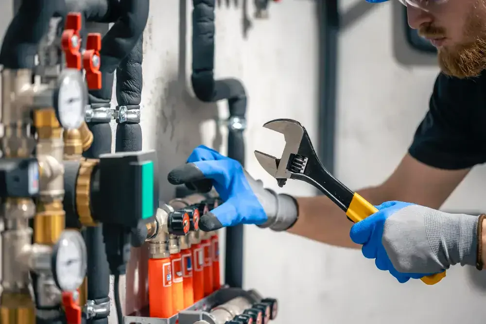 A technician wearing blue gloves is using a wrench to work on a complex system of pipes, gauges, and valves.