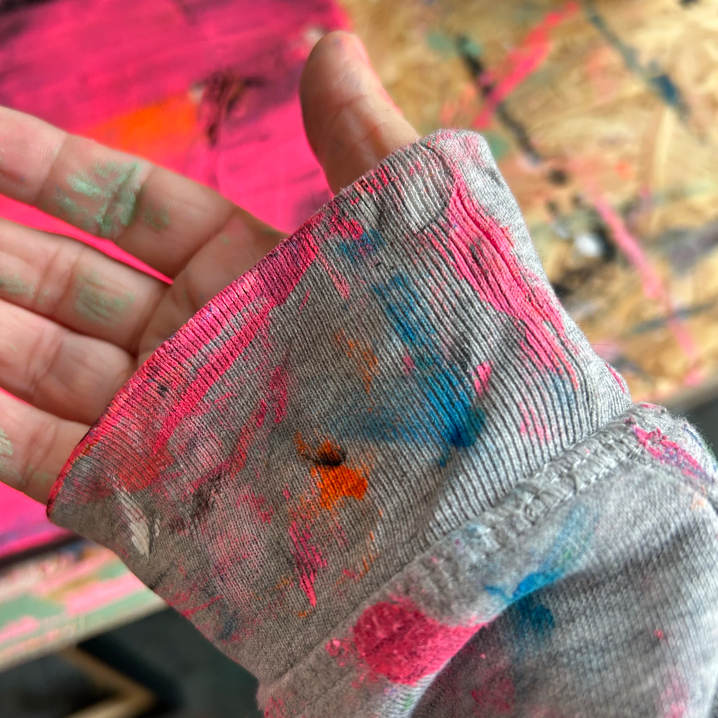 Nahaufnahme einer Hand mit bunter, schmutziger Arbeitshandschuh, der auf einem bunten, spraybemalten Hintergrund liegt.