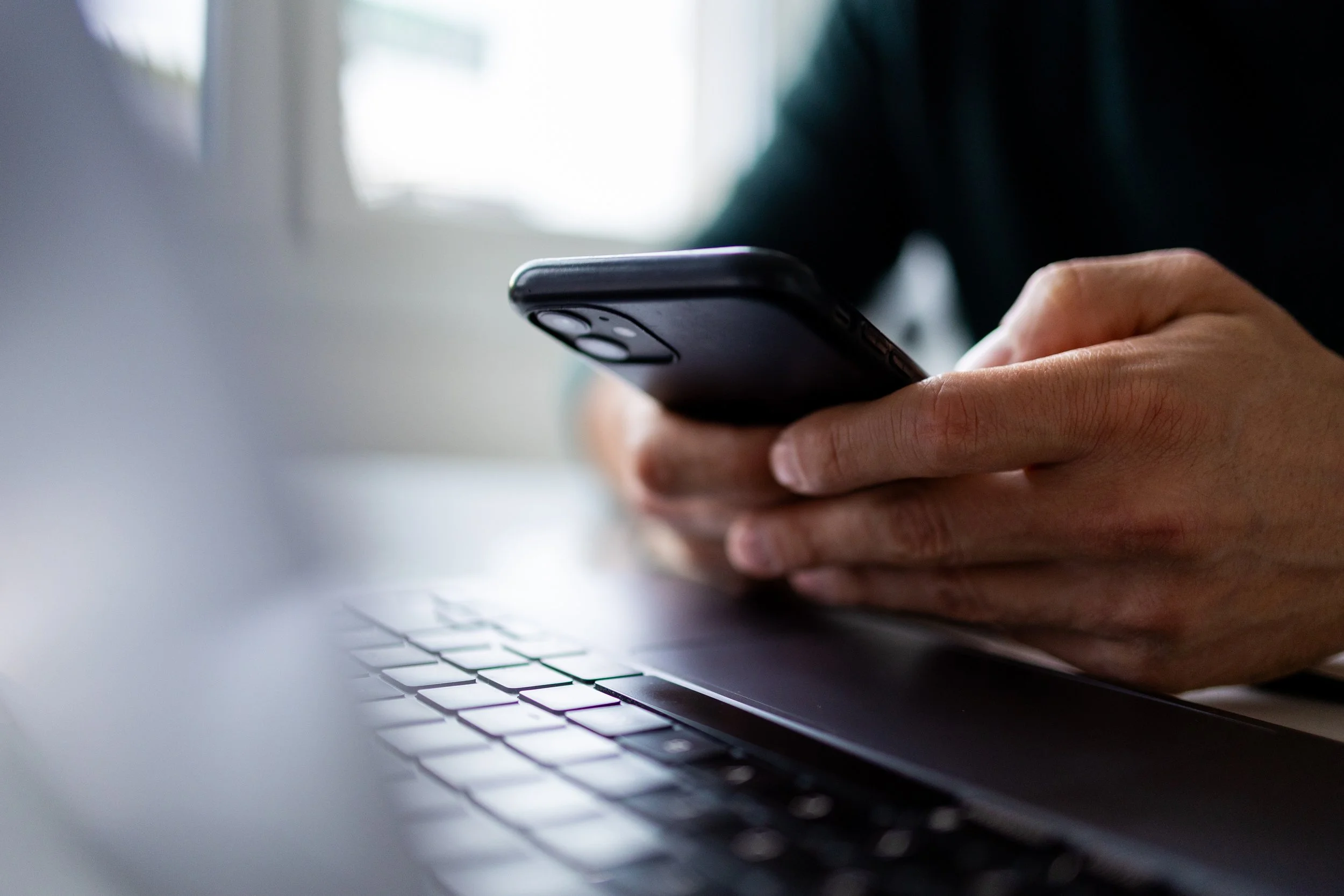 Close-up of a person's hand holding a smartphone over a laptop keyboard.