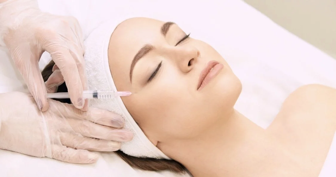 A woman receiving a cosmetic injection on her face in a medical setting.