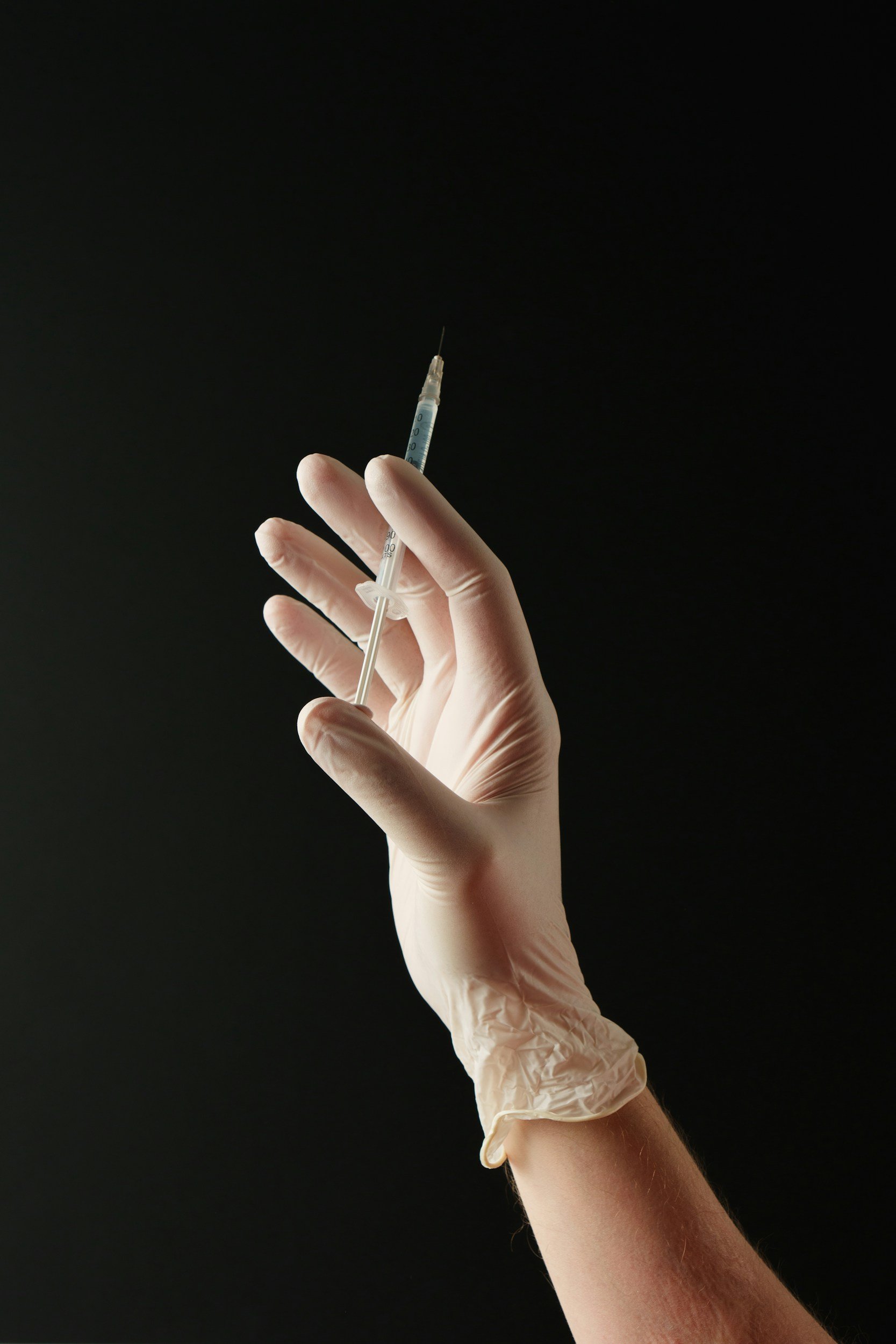 A gloved hand holding a syringe against a dark background.