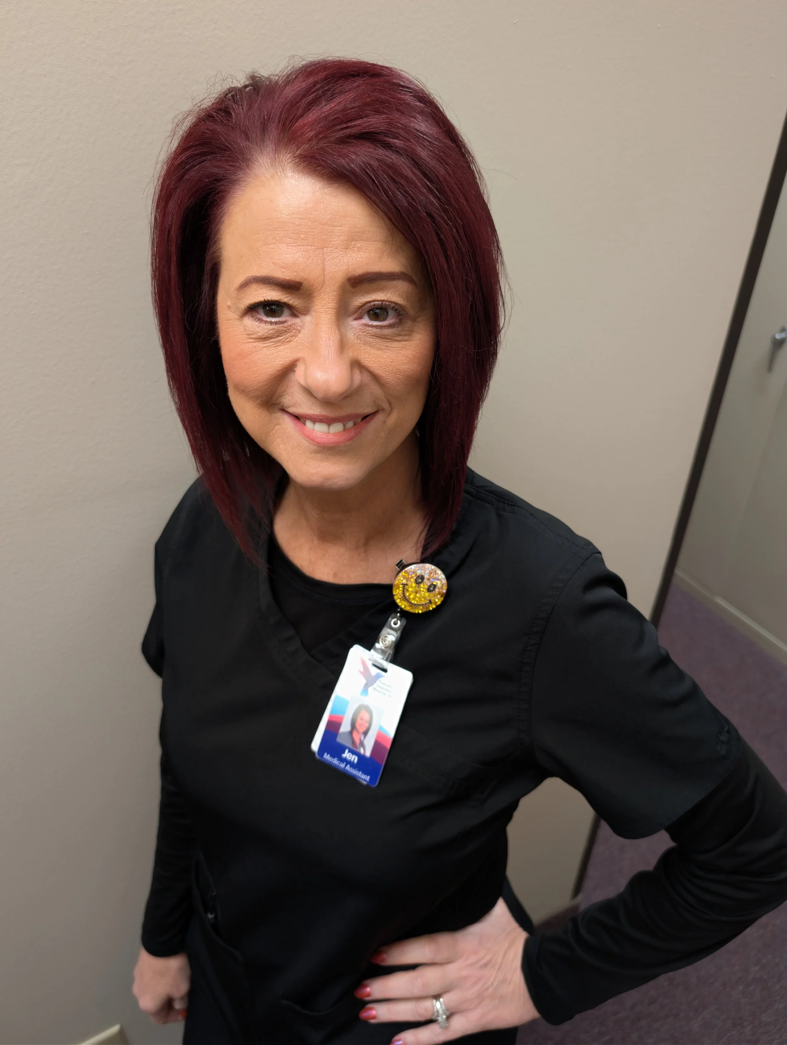 Portrait of a woman with colorful hair standing in front of a mirror in a room with blue walls.